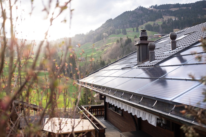 Dach mit Kamin und Solaranlage, im Hintergrund eine ländliche, hügelige Gegend