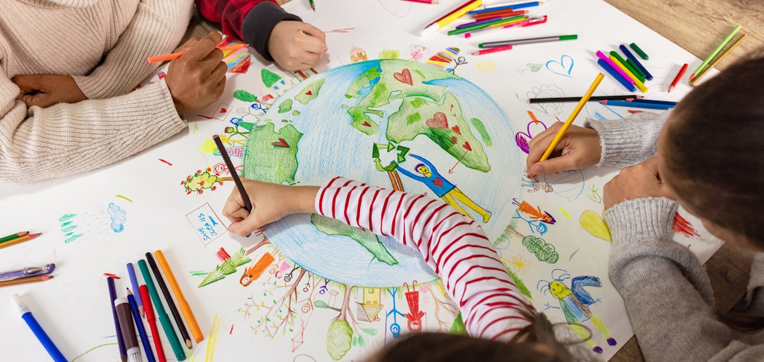 Bildung für Nachhaltige Entwicklung Kinderhände zeichnen zusammen ein Plakat, das die Welt mit vielen Figuren, Bäumen und Herzen zeigt