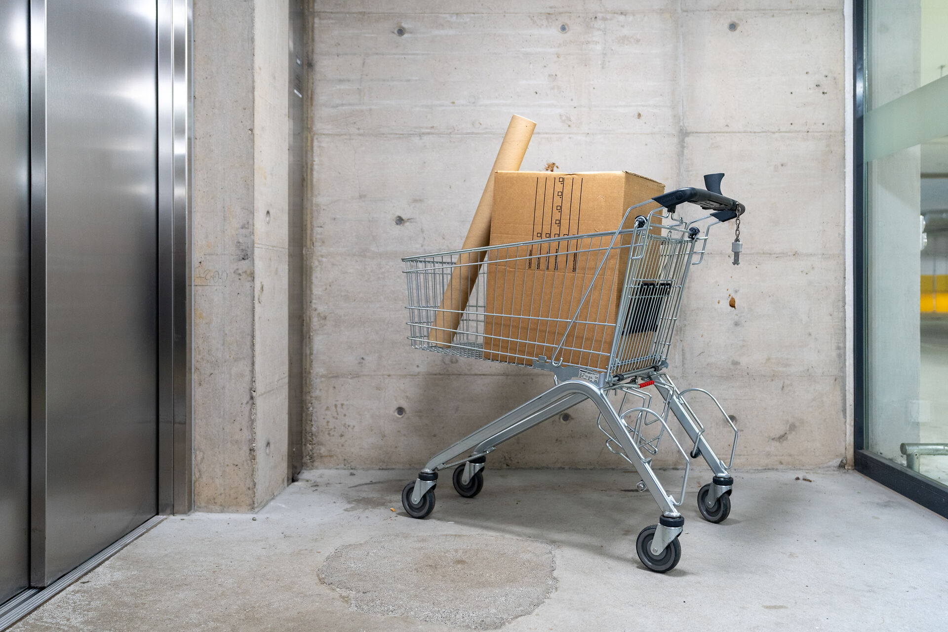 Einkaufswagen steht vor einem Warenlift, darin liegen zwei Pakete.