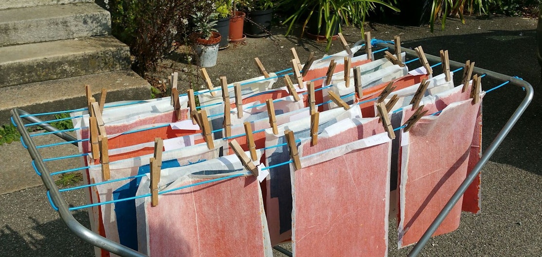 Papierschöpfwerkstatt Wäscheständer, an dem rotes und blaues Papier zum trocknen hängt