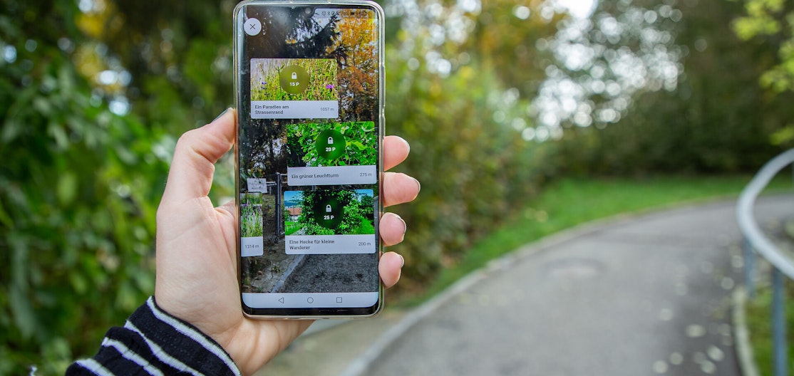 Naturpade-App im Einsatz Eine Hand hält ein Smartphone hoch, auf dem die Naturpfade-App geöffnet ist