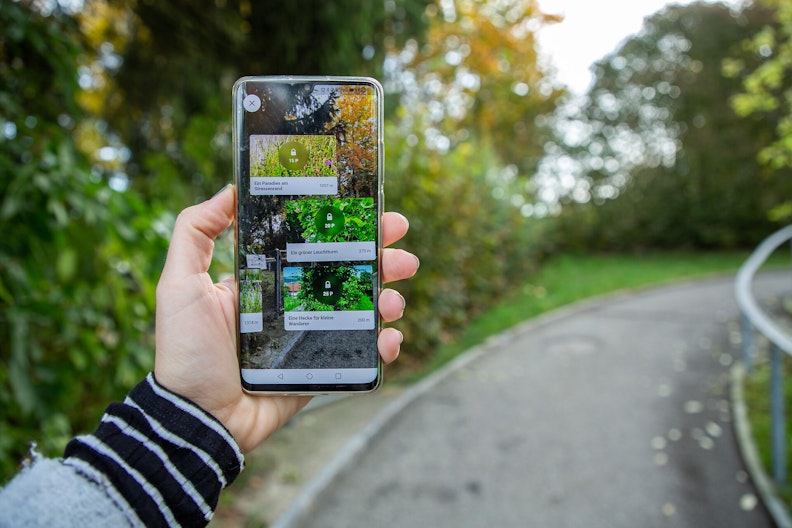 Eine Hand hält ein Smartphone hoch, auf dem die Naturpfade-App geöffnet ist