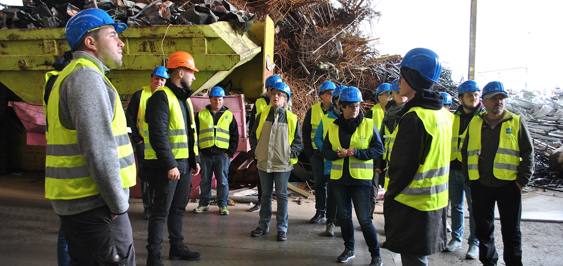 Kursteilnehmende in der Sammelstelle Kursteilnehmende mit gelber Warnweste und blauen Schutzhelfen stehen in einer Sammelstelle vor einem Abfallberg