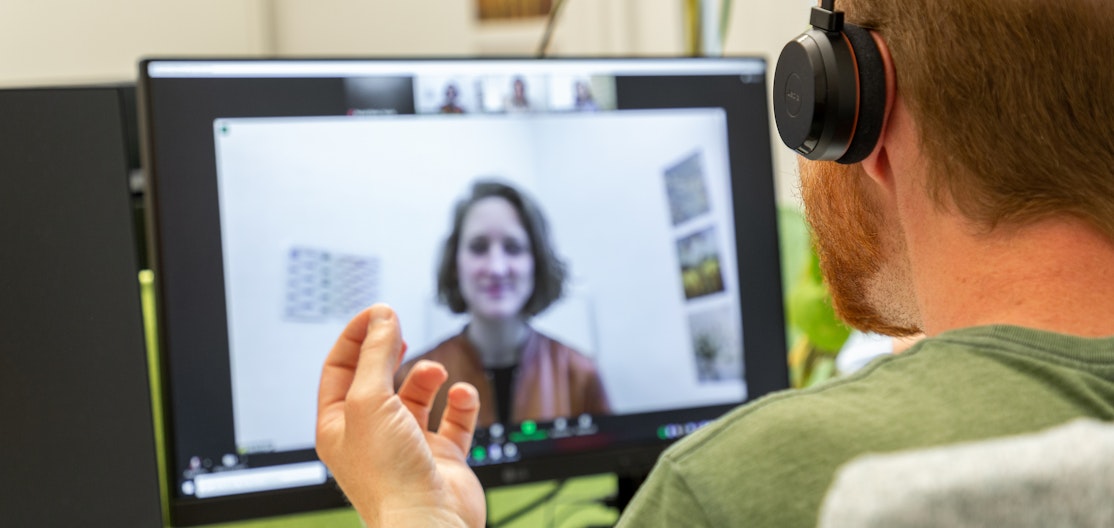 Hotline Klimastrategie Ein Mann mit Headset sitzt vor dem Computer und führt eine Beratung durch. Auf dem Bildschirm ist unscharf eine Teilnehmerin zu erkennen.