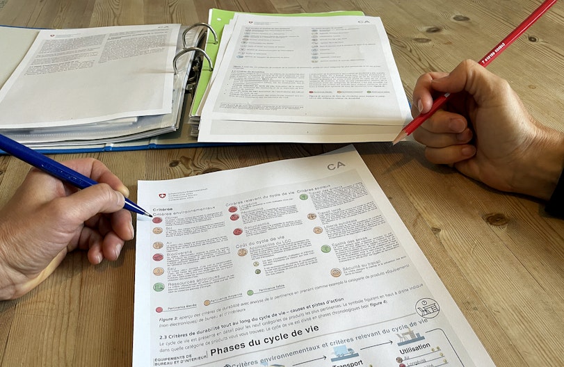 Un document de la confédération expliquant les critères d’achats publics responsables. Une main tient un crayon, prête à prendre des notes.