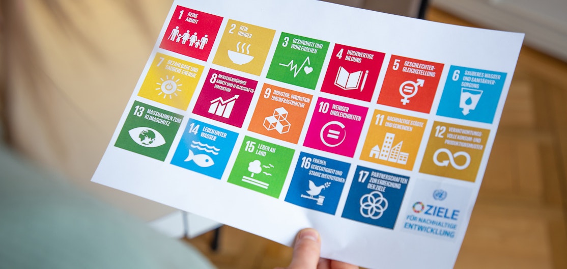 SDG Ziele Eine Person hält ein Blatt auf dem die 17 SDG Ziele abgebildet sind.