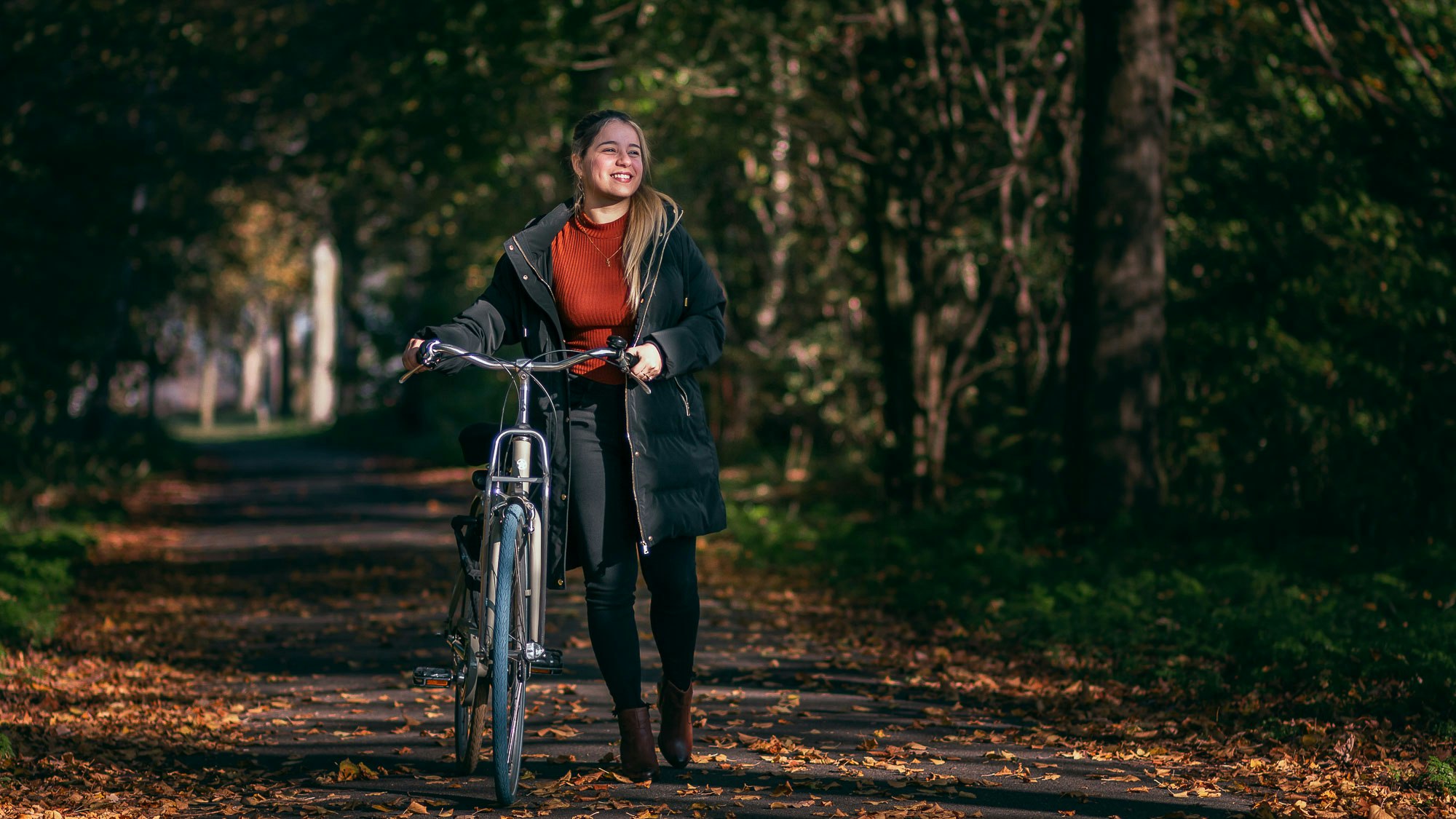Lisandra walking her bike among trees