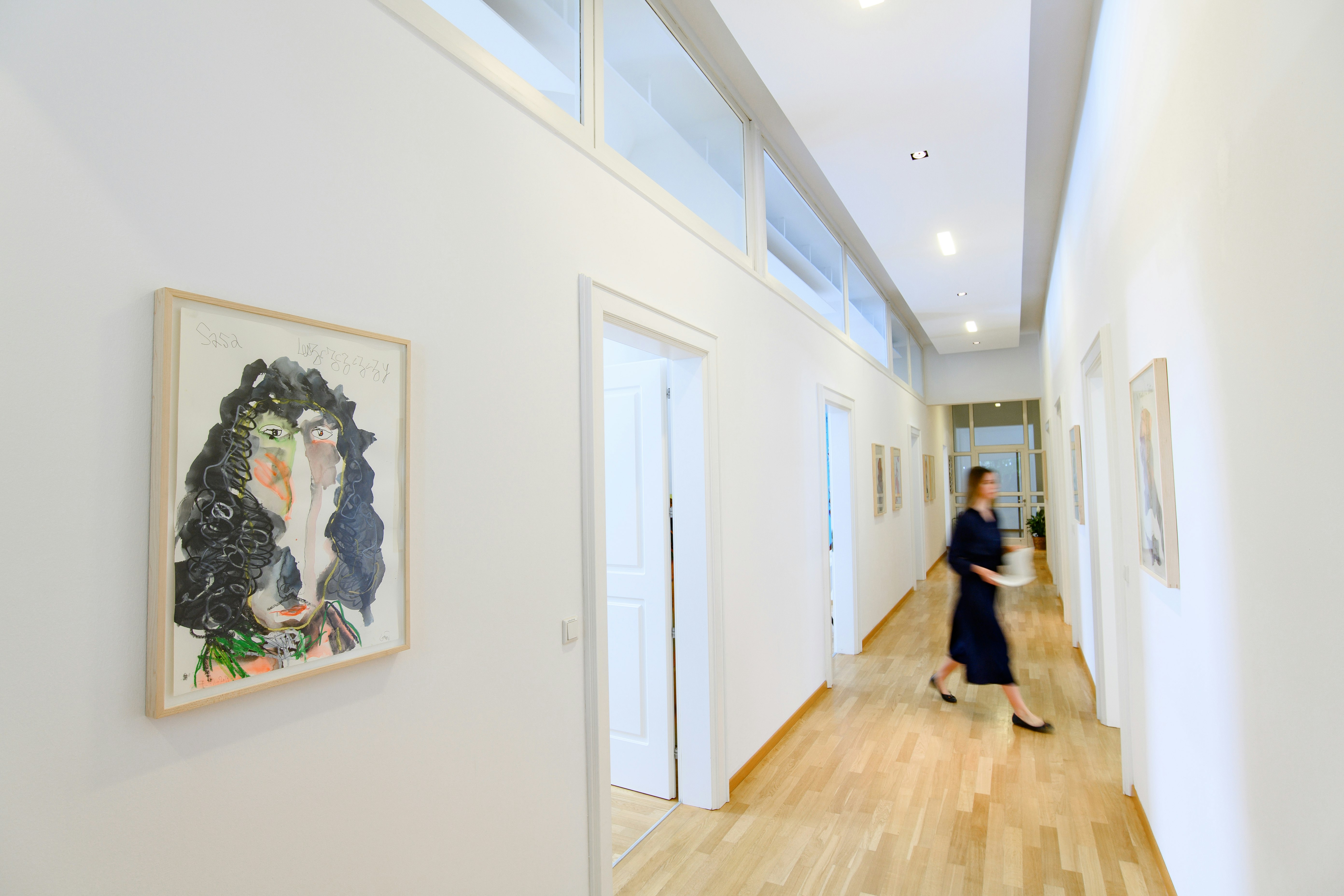 Corridor of the office in Munich, with an arts piece on the left wall and a woman crossing from room to room