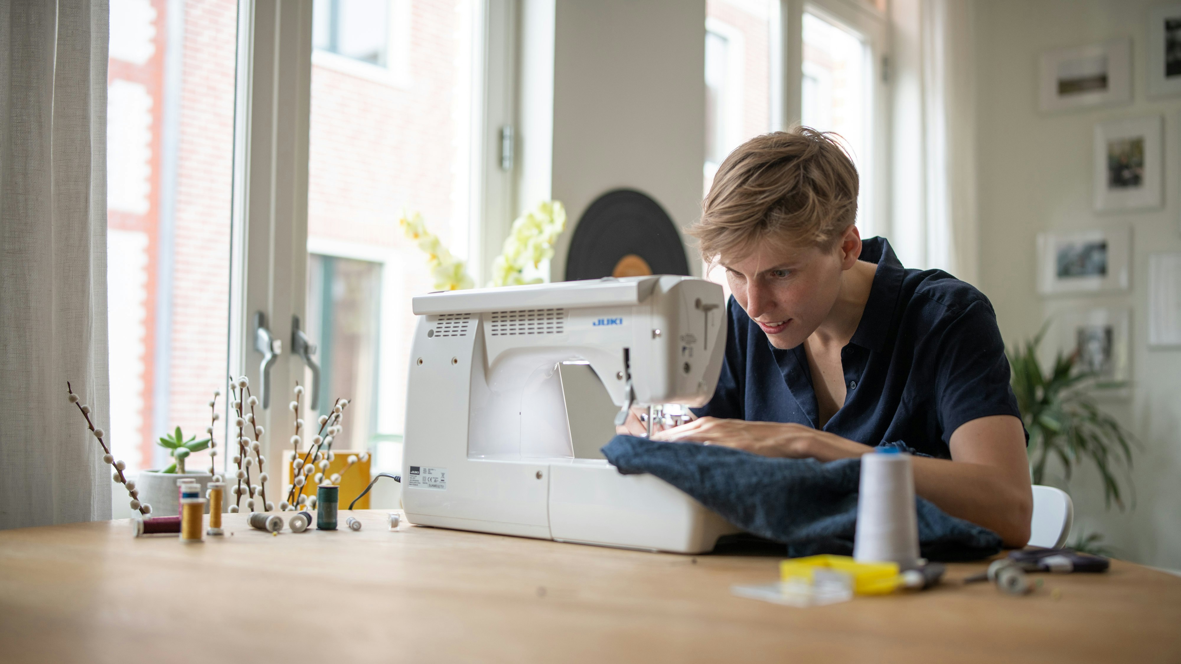 Annegret Bönemann at home, in a blue shirt, sewing a blue fabric with a machine