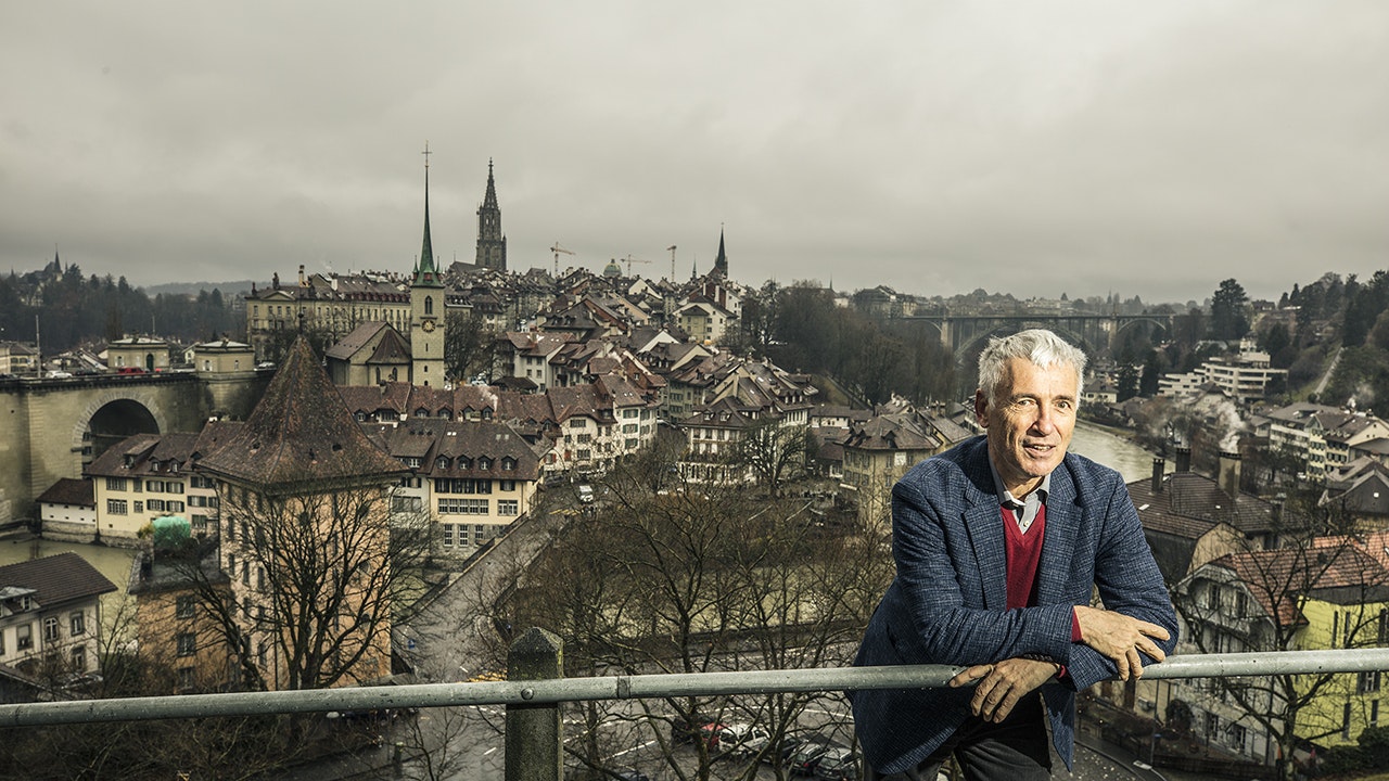 Man in suit leaning on a railing, the city of Bern in the background