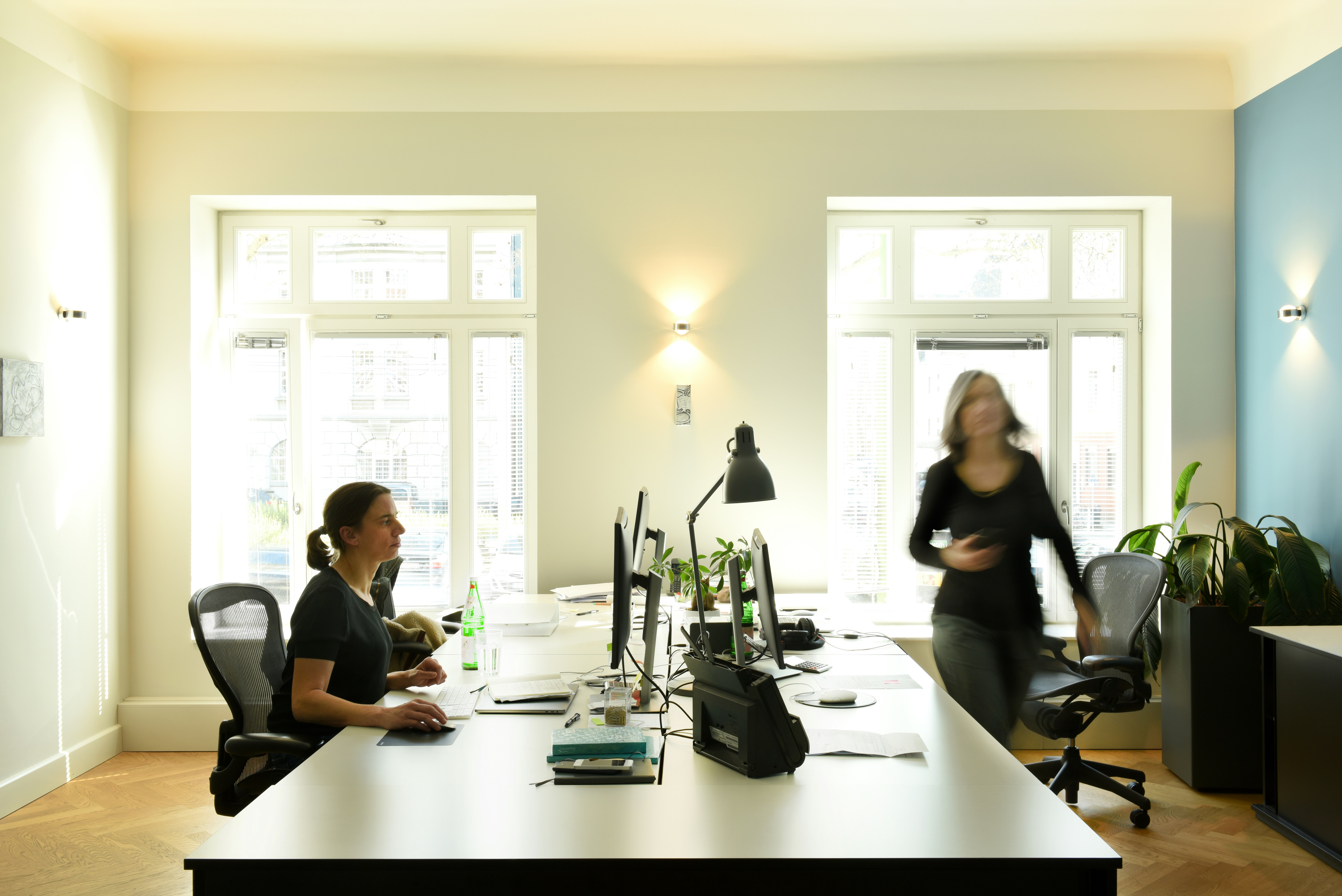 Zwei Frauen an ihrem Arbeitsplatz in einem Büro in Essen mit hellen Fenstern.