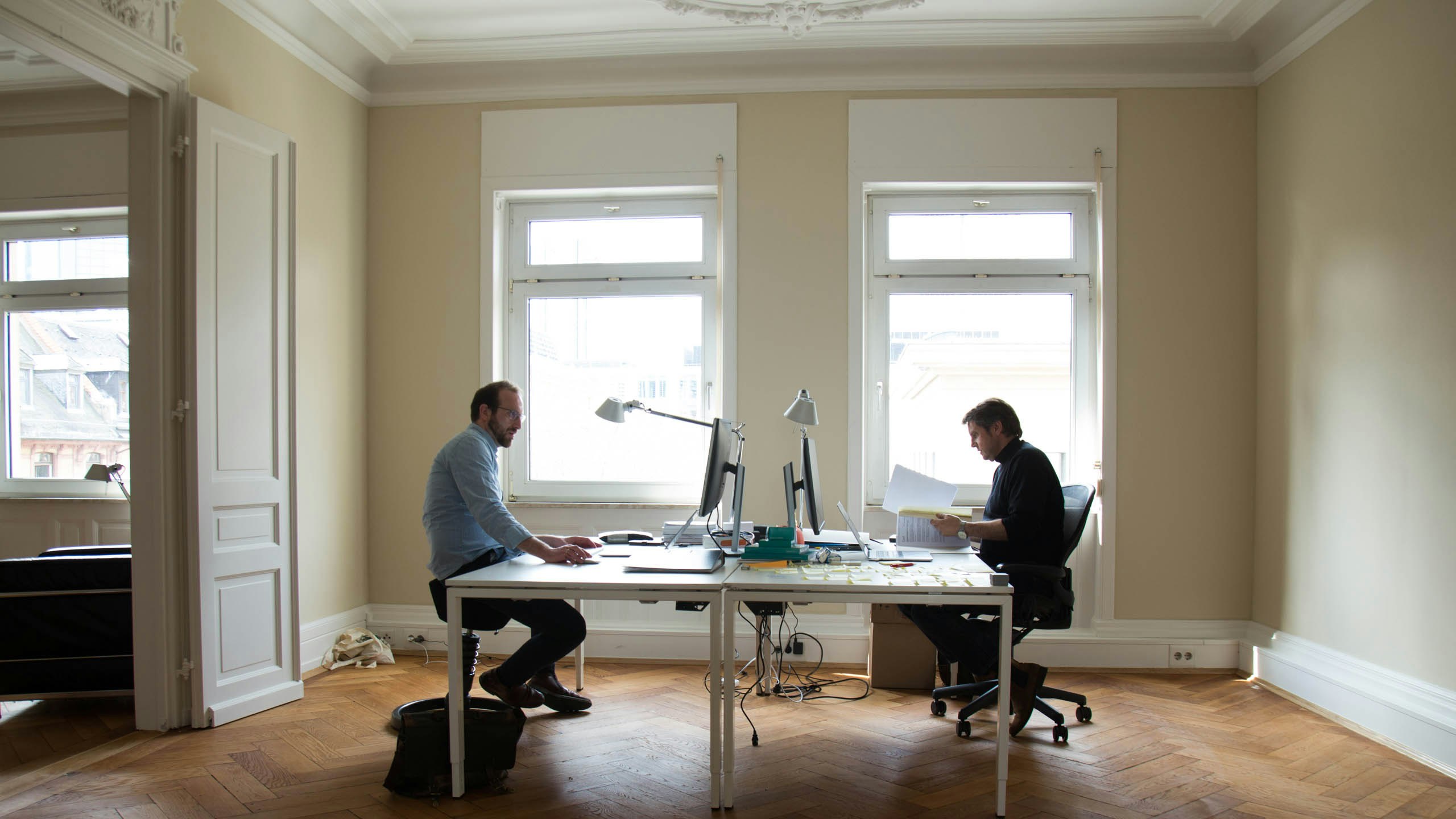 Werner Spengler und Andreas Gutheil sitzen hinter ihrem Schreibtisch in ihrem Büro mit hellen Wänden und Fenstern.