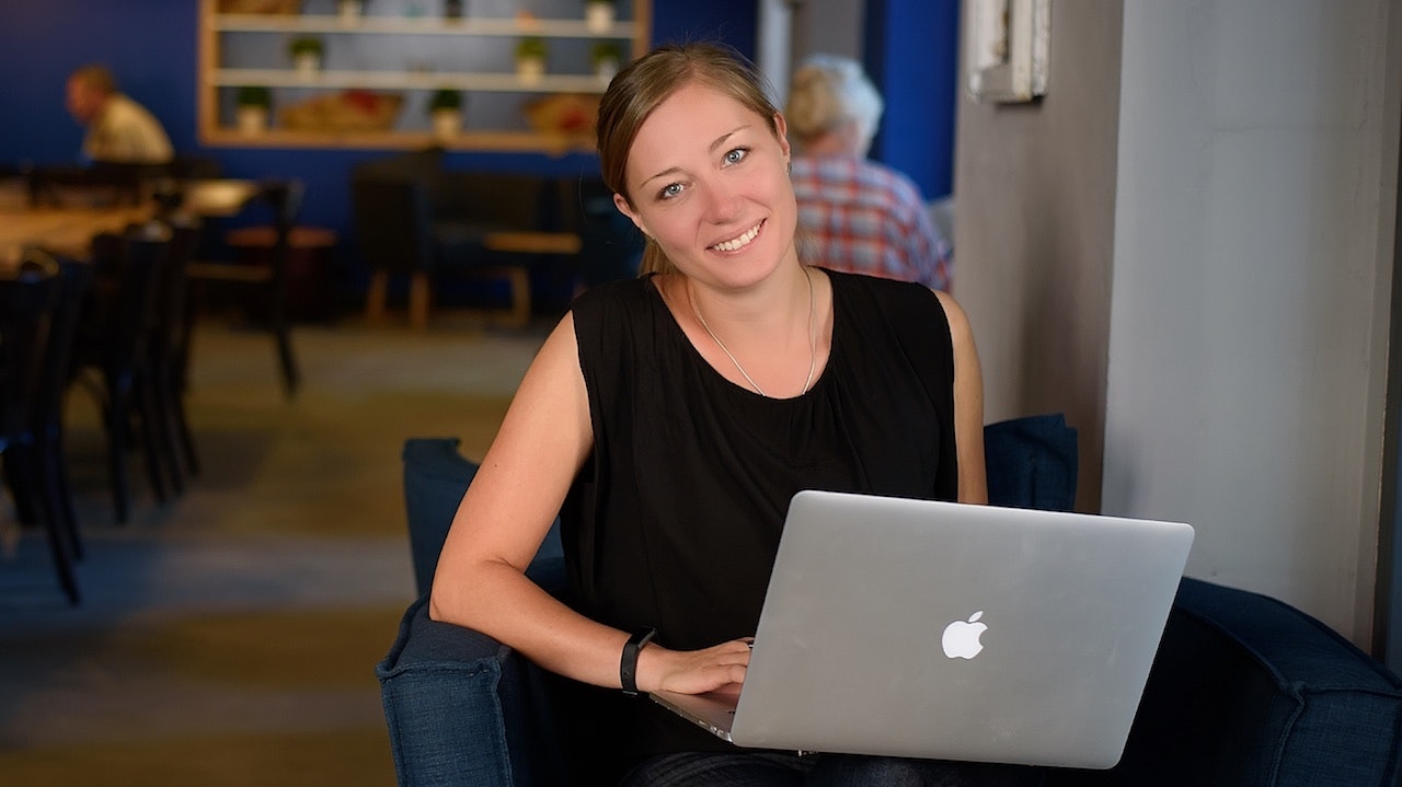 Albena Mancheva sitting in a cushioned chair with open laptop smiling..