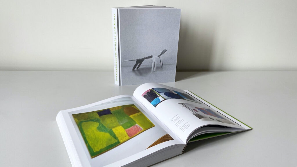 Aufgeschlagenes Buch "Unternehmensphilosophie und Kunst" mit Kunst auf beiden Seiten auf einem Tisch