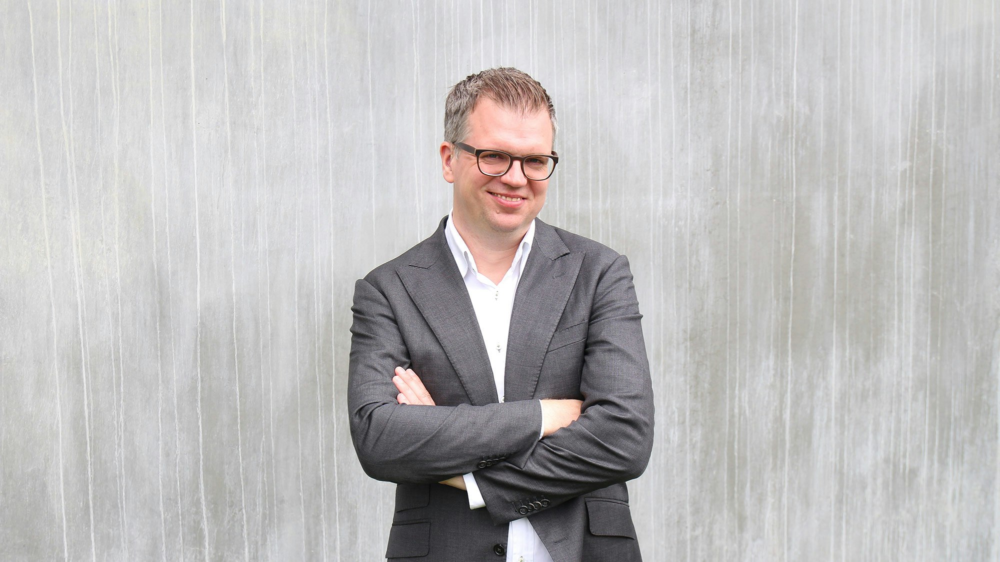 Jonathan Möller in grauem Anzug, lächelnd vor einer grauen Wand