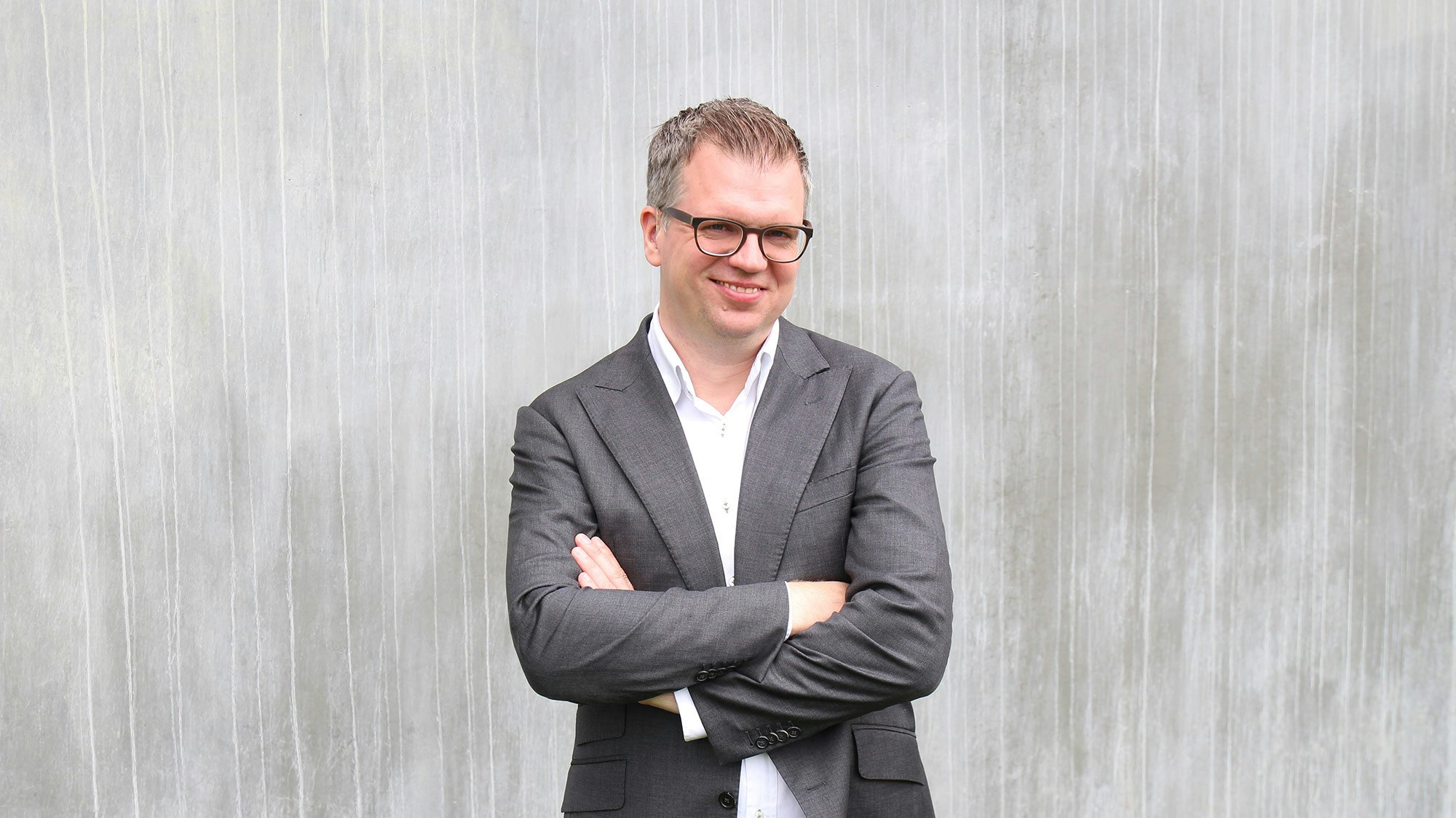 Jonathan Möller in a gray suit, smiling in front of a gray wall