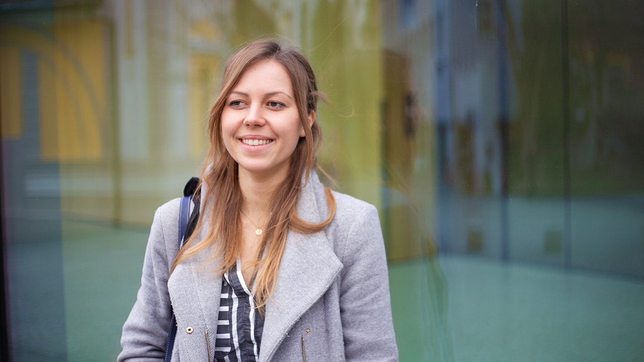 Johanna, smiling, in a grey coat against a blurred background.