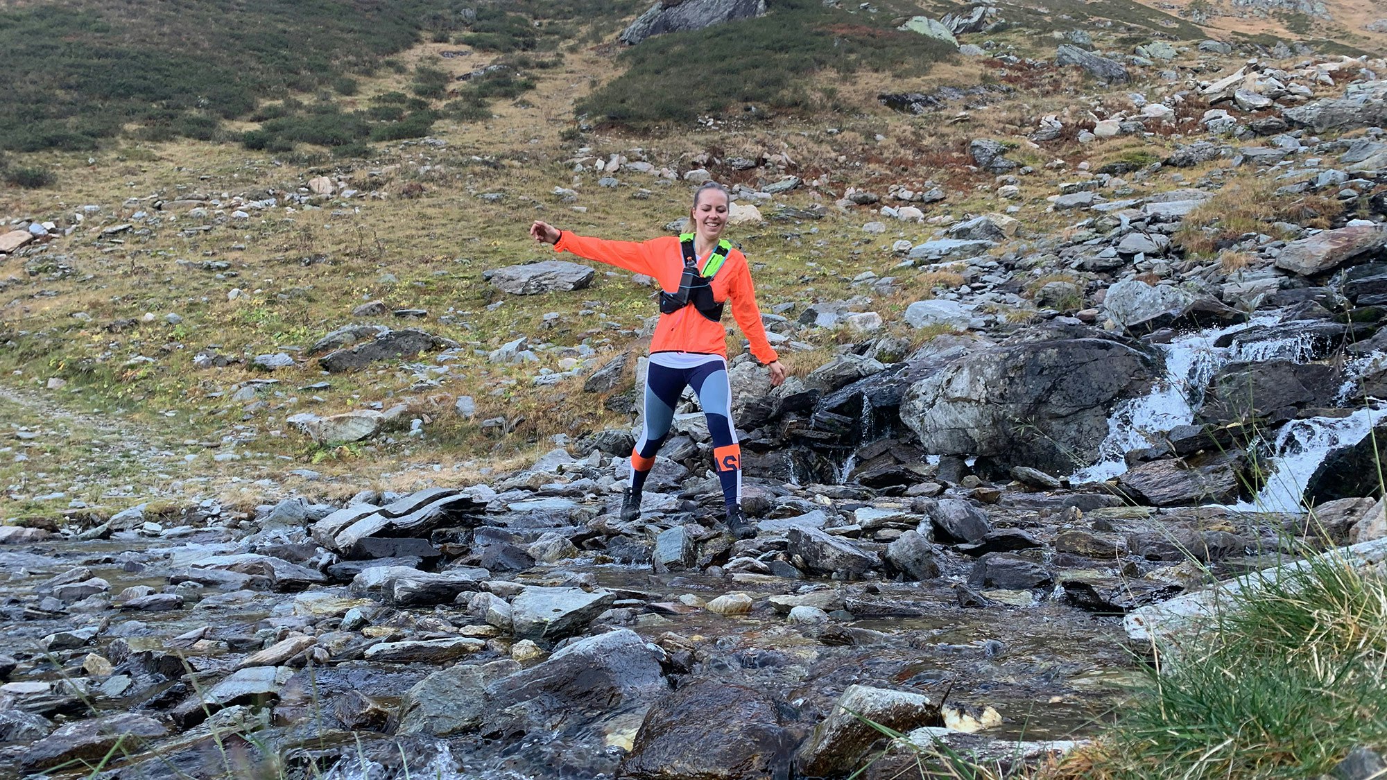 Johanna, in a sporty outfit, runs over stones in the mountains.