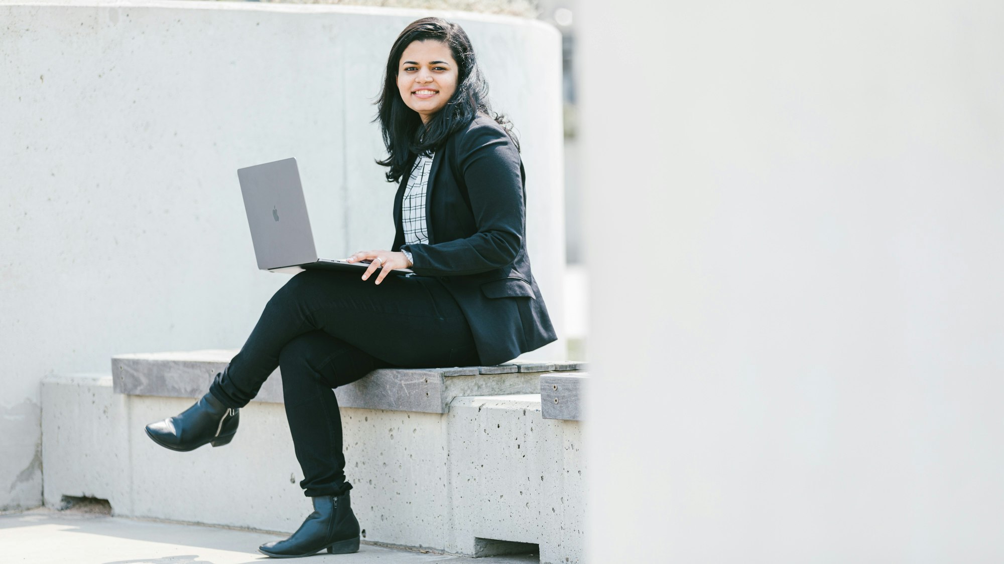 Tissa sitting on a stone city bench with her open laptop on her lap.