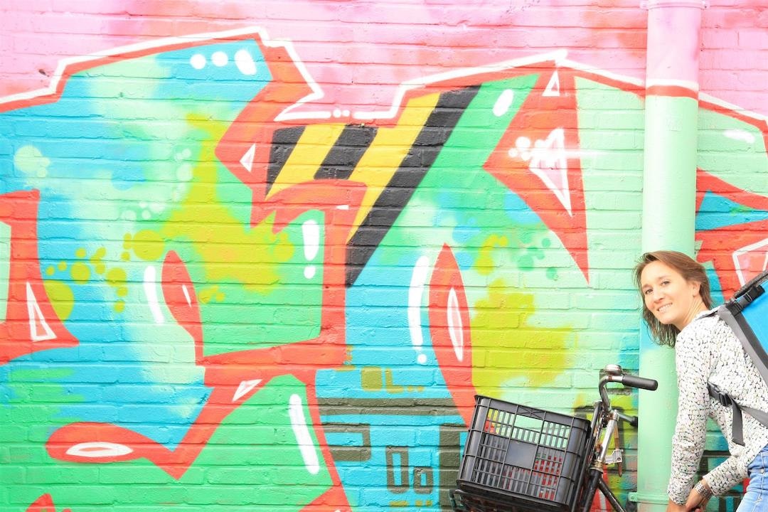 Valerie is with her bike showing a bright graffiti wall.