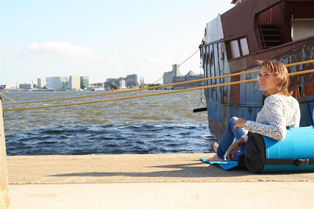 Valerie is sitting on a dock next to an old boat, with Amsterdam skyline in the background.