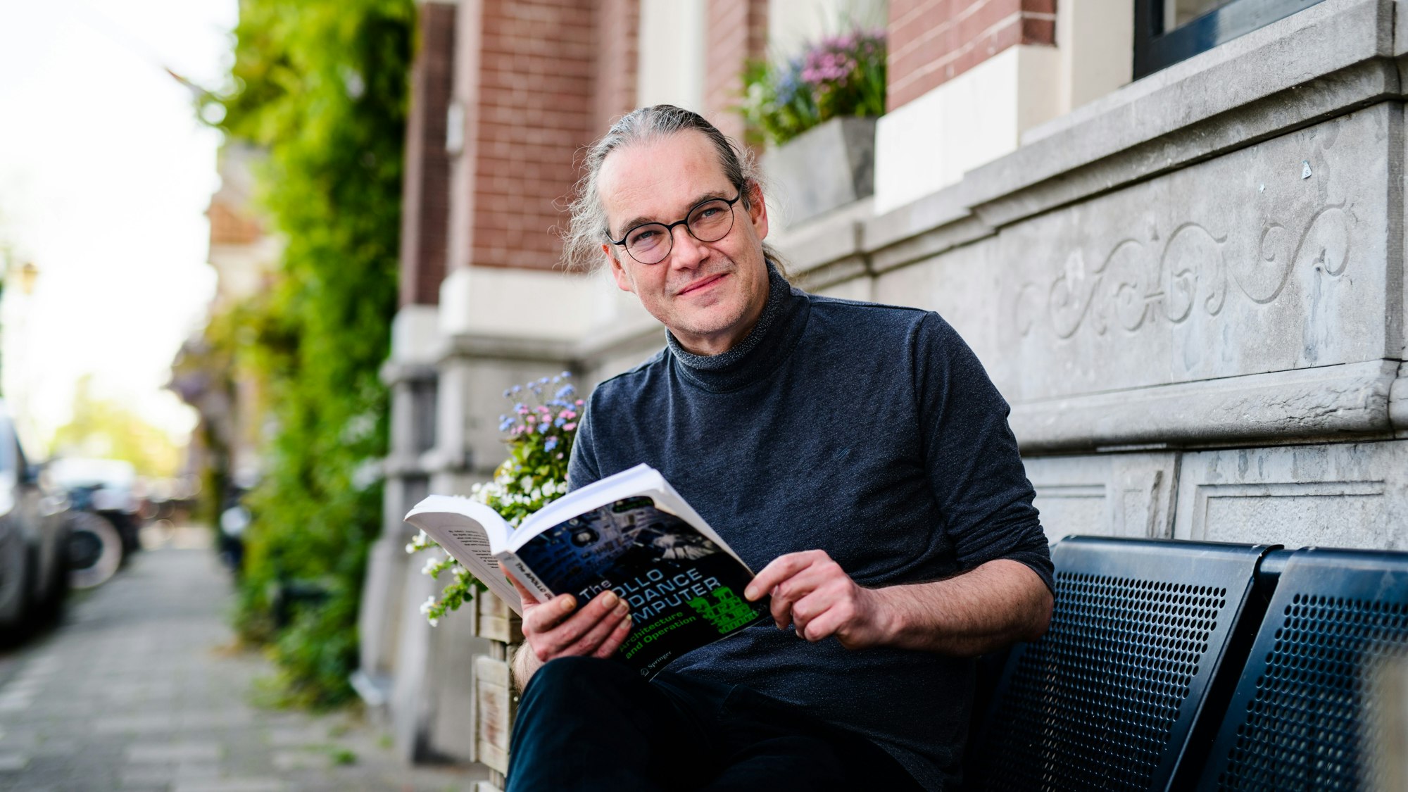 Edwin sitting on a bench in front of an Amsterdam house with a book in his hands.