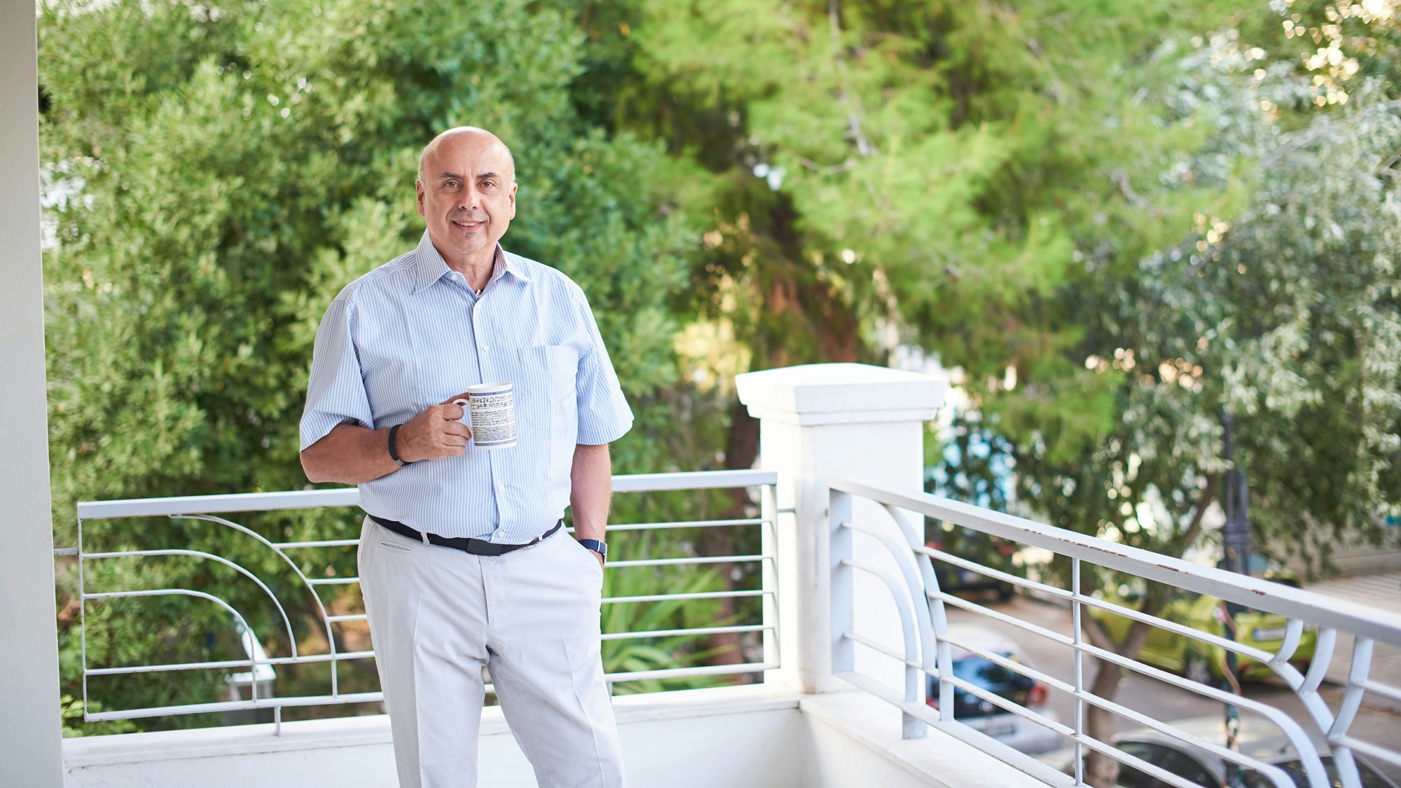 Antonios with a cup of coffee in his hand on terrace outside.