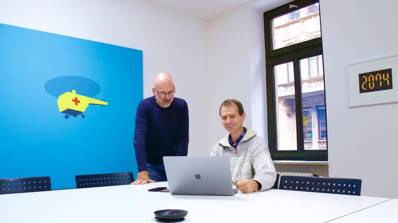 The CEO Andreas Drexhage and his deputy Rainer Fauth in the office next to an art piece depicting a yellow helicopter on blue background.