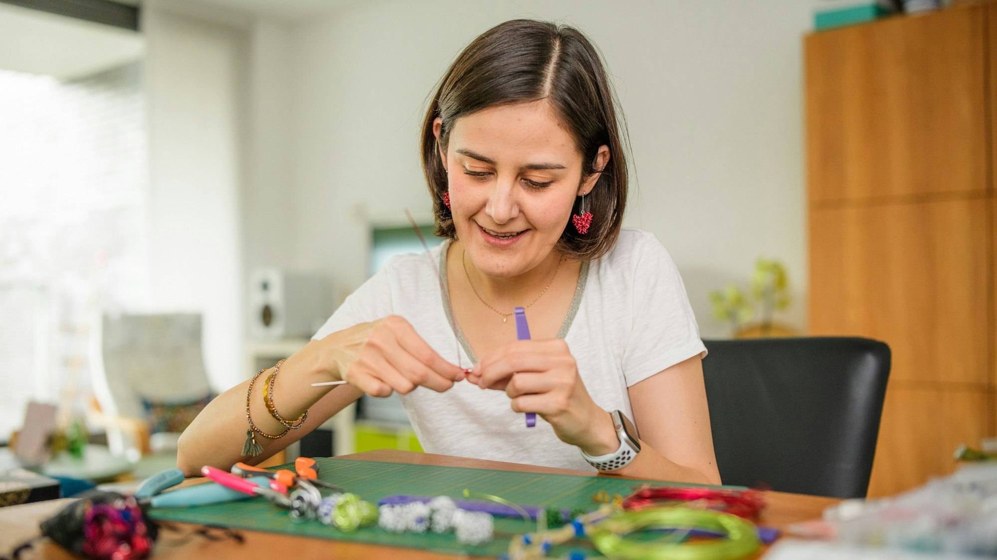 Een jonge glimlachende vrouw met haar tot op de kin, die sieraden maakt.
