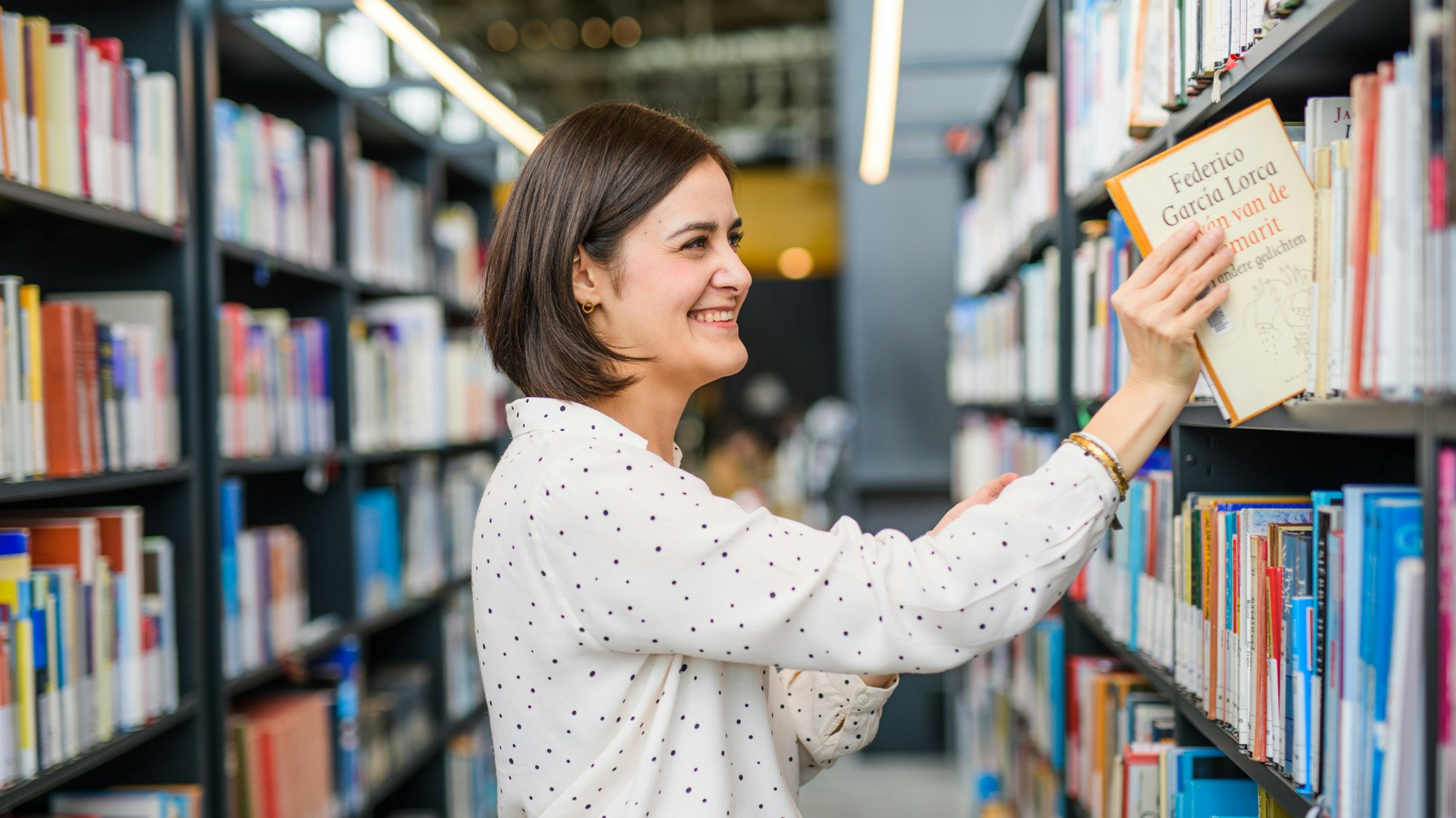 Cristy in een bibliotheek, plaatst een boek van Federico Garcia Lorca op een plank