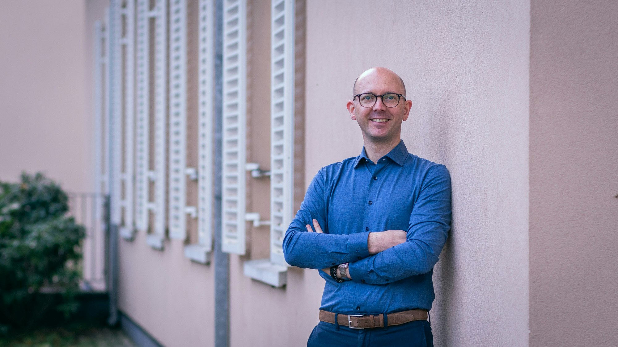 Mann in blauem Shirt, lehnt an Wand und lächelt