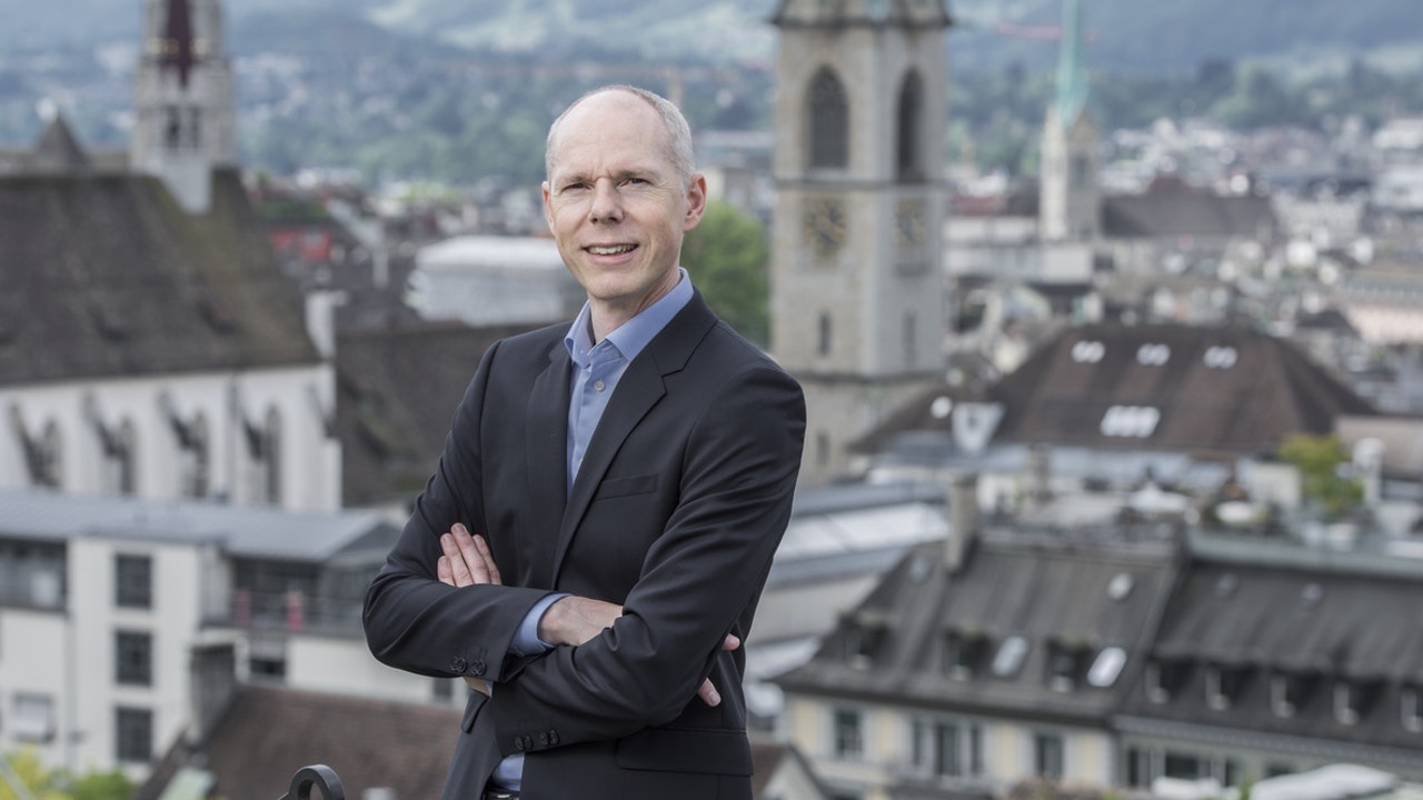 Man in dark suit in front of city panorama