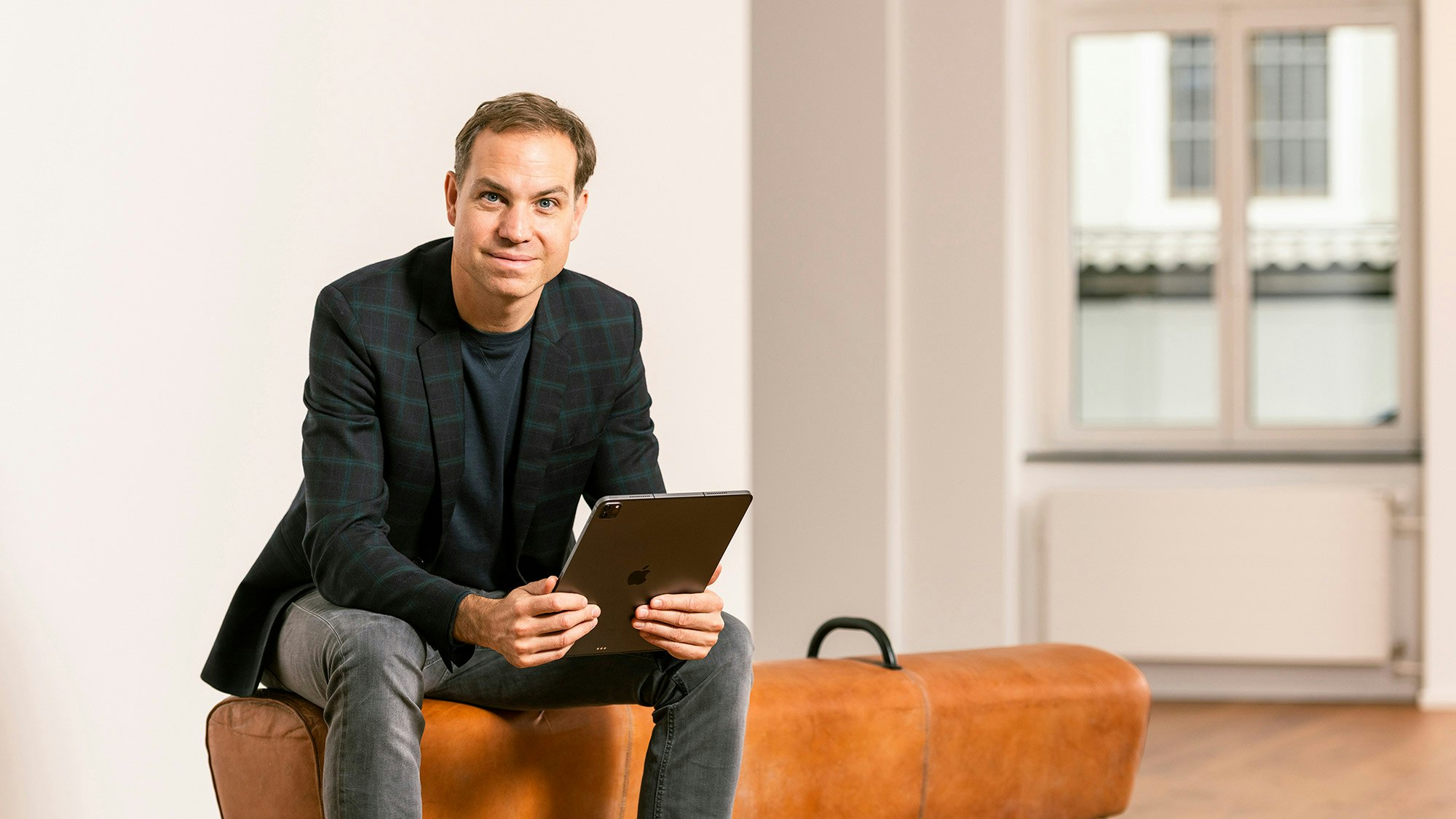 Profilbild von Tobias Felbecker, der auf einer orangefarbenen Bank sitzt und ein iPad hält.