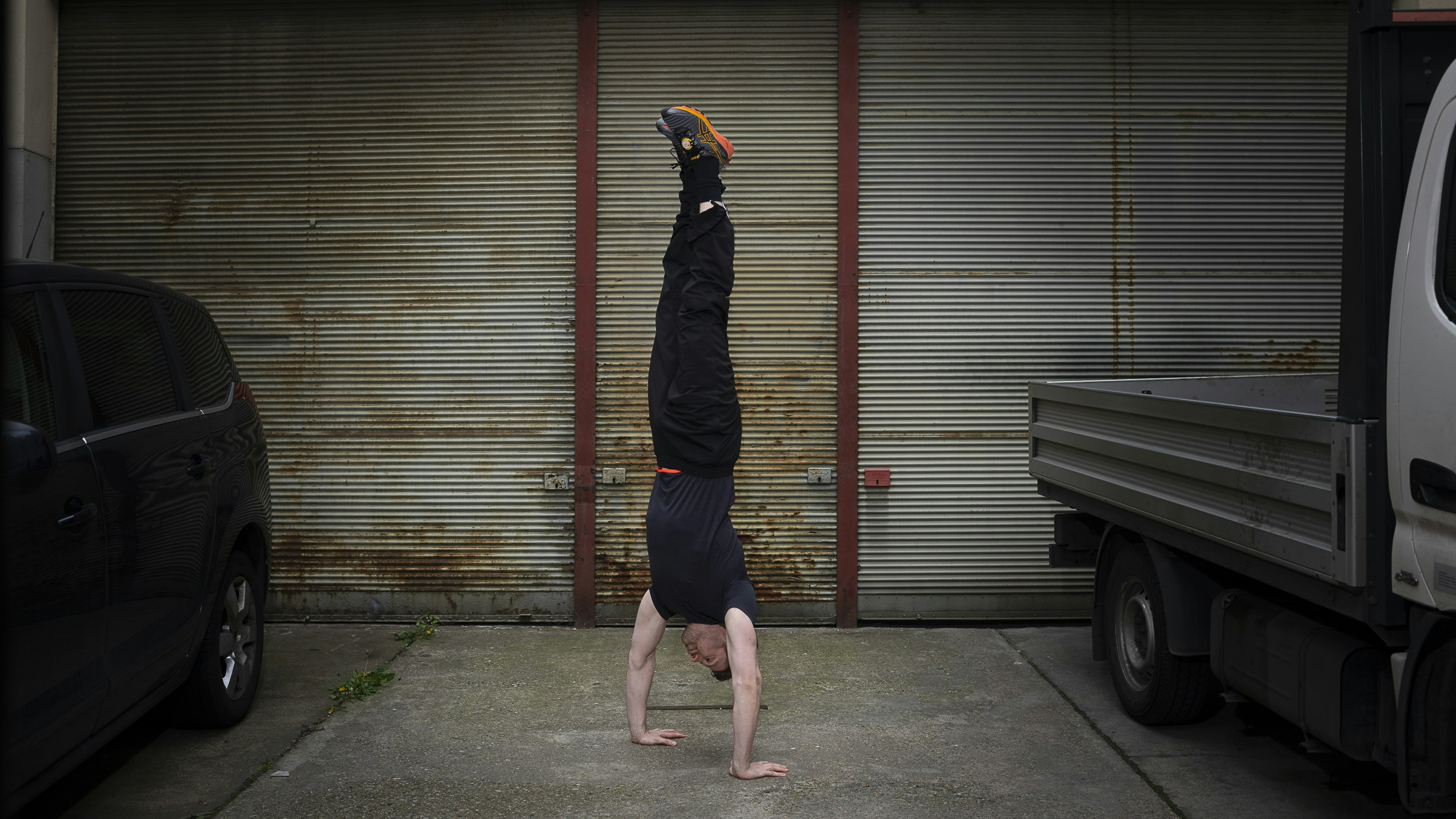 Manual Hanel doing a handstand among two cars in a garage.