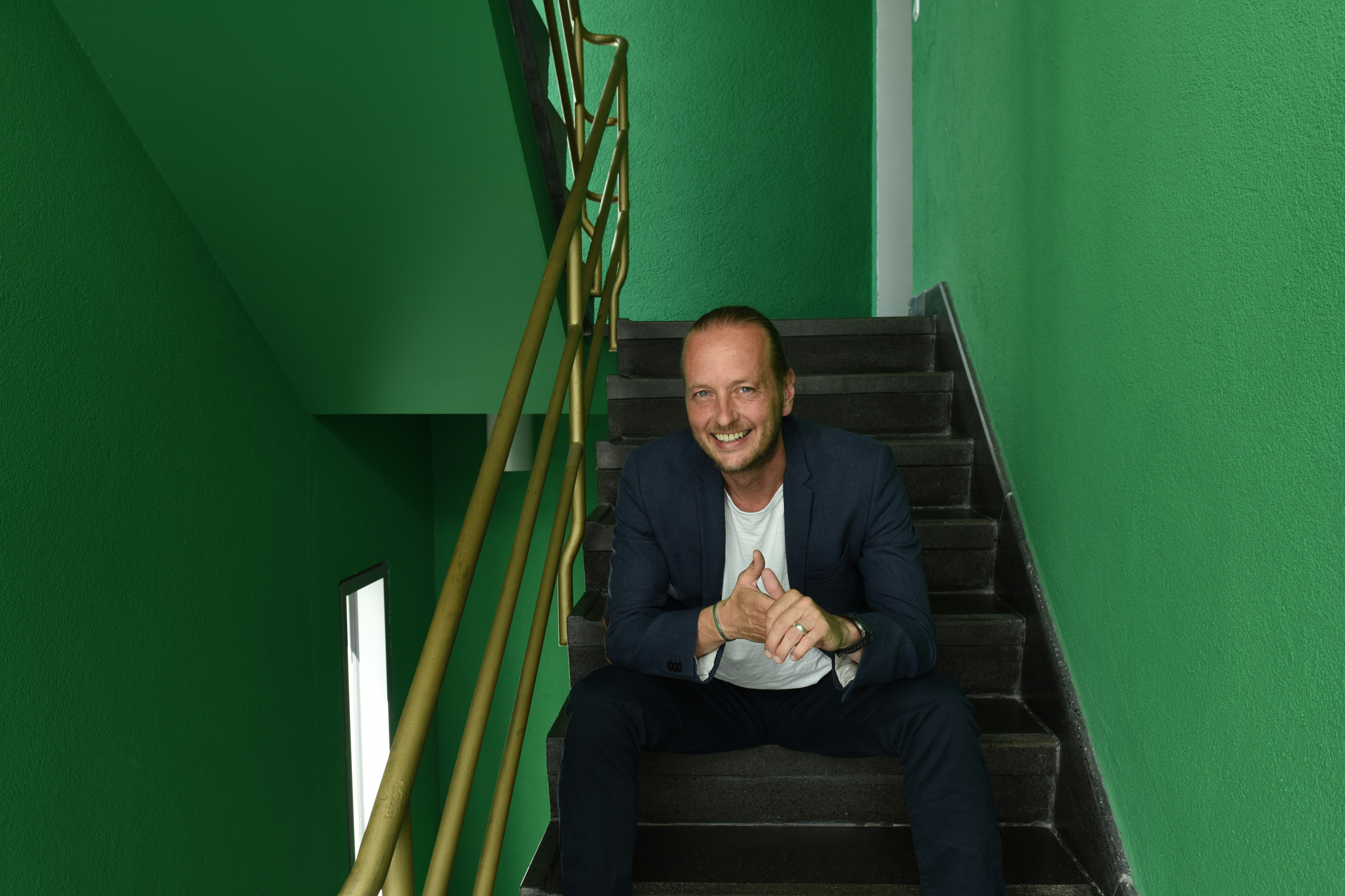 Hannes Benjamin Weikert sitzt in einem Treppenhaus mit grünen Wänden.