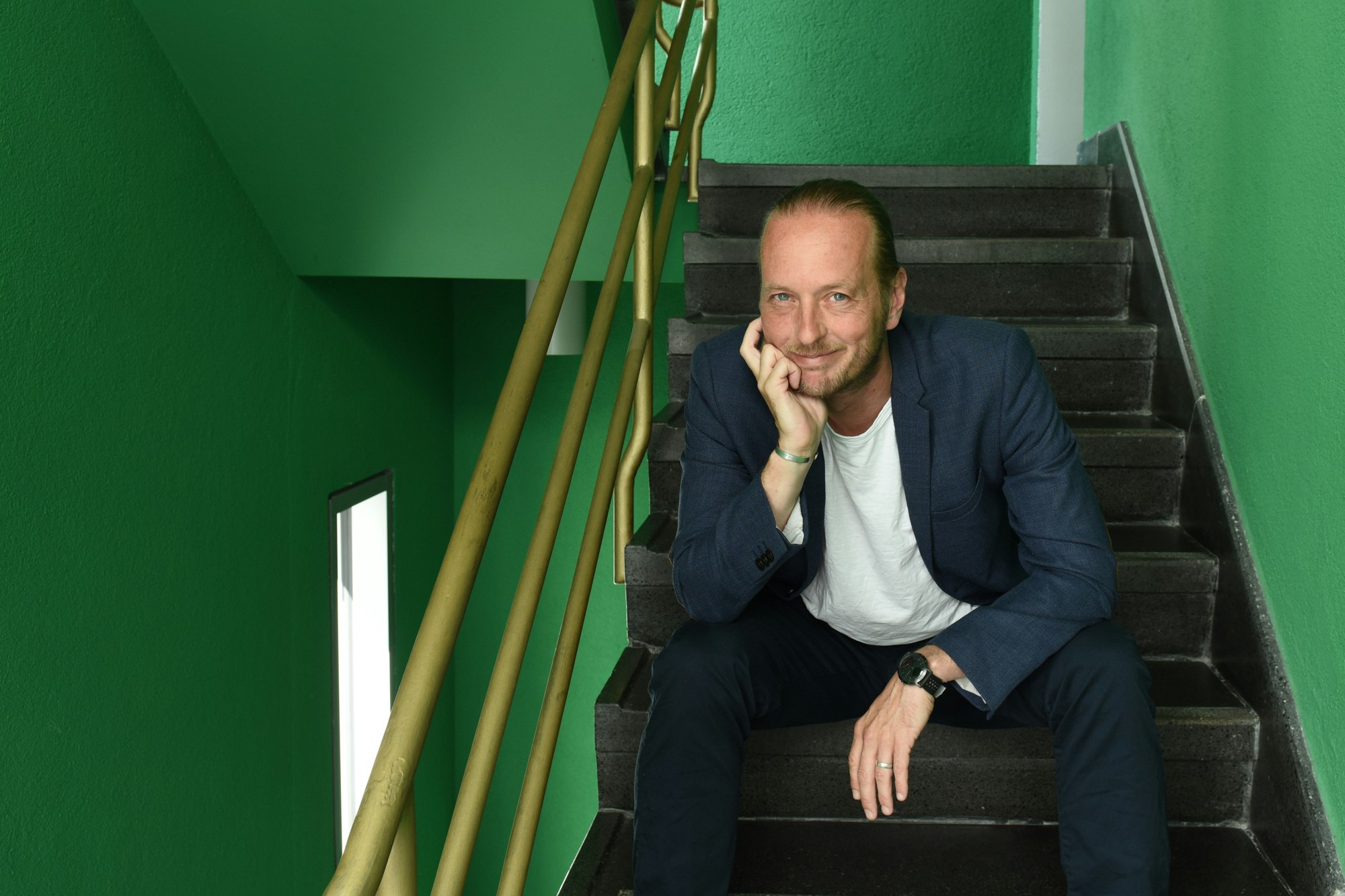Hannes Benjamin Weikert sitzt in einem grünen Treppenhaus.