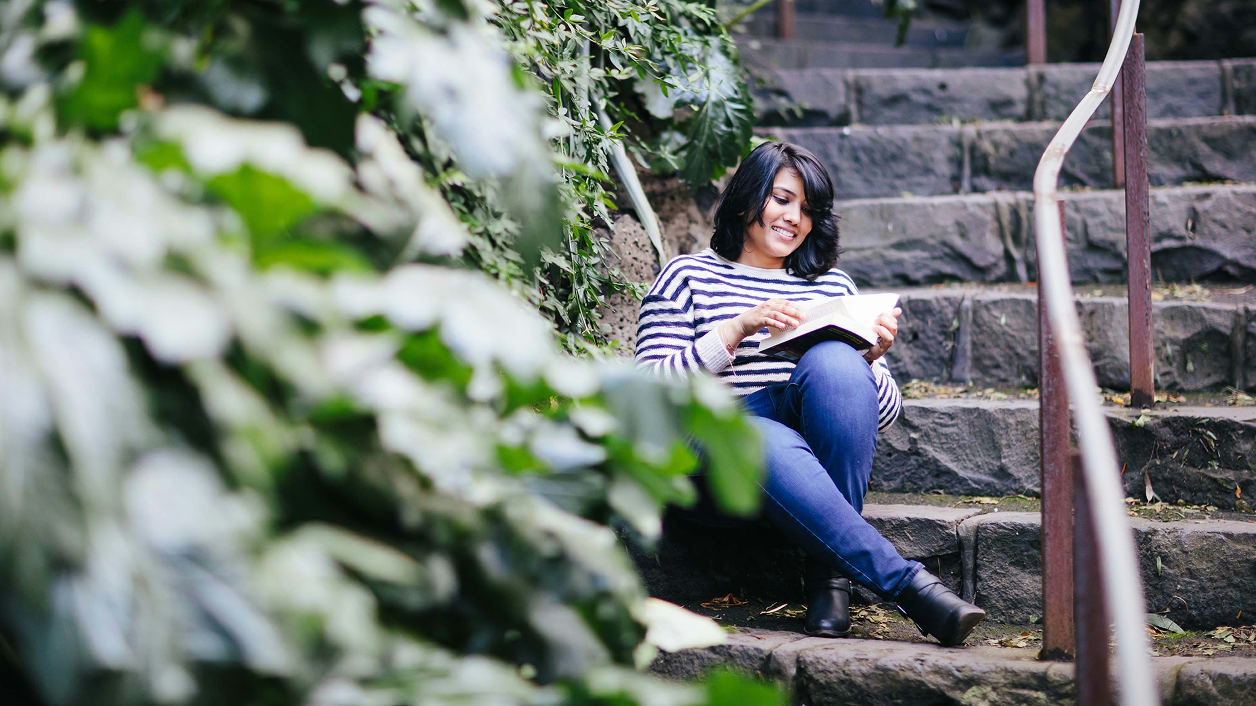 Femila Jesline reading a book on an outside stone staircase