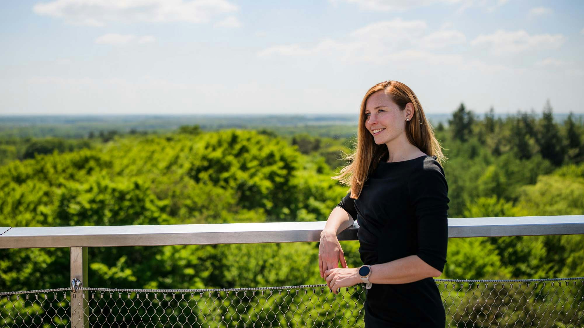 Jana Šlechtová at a viewing point overseeing a bright green forest.
