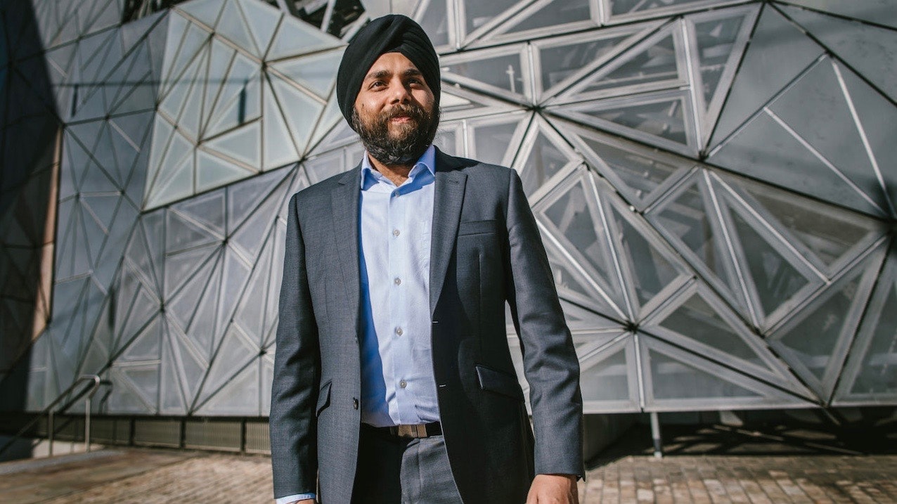 Randeep Gandhi in a suit in front of a glass structured building.