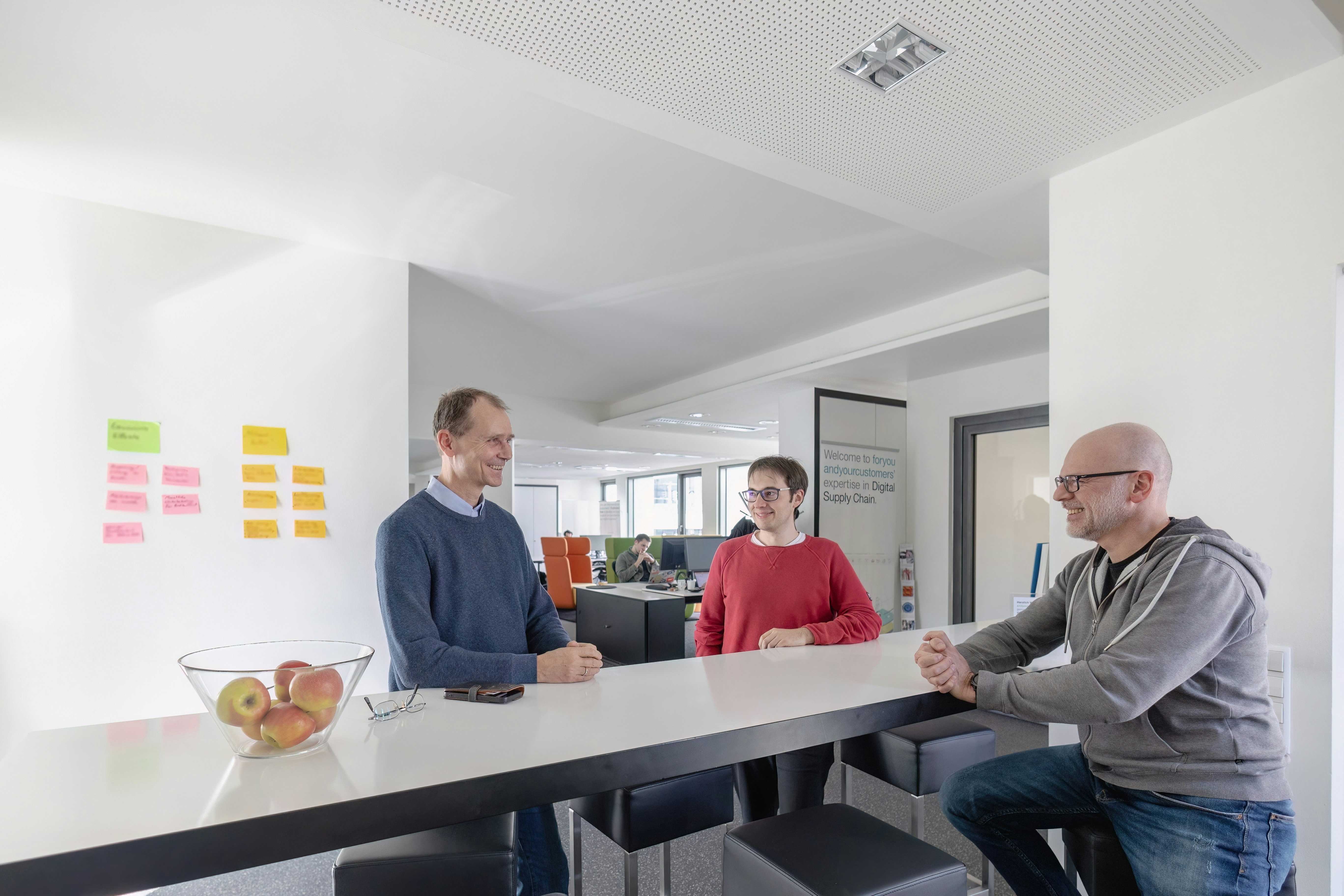 Managing director Andreas Drexhage talking with two colleagues. They are standing around a bar table in an office.