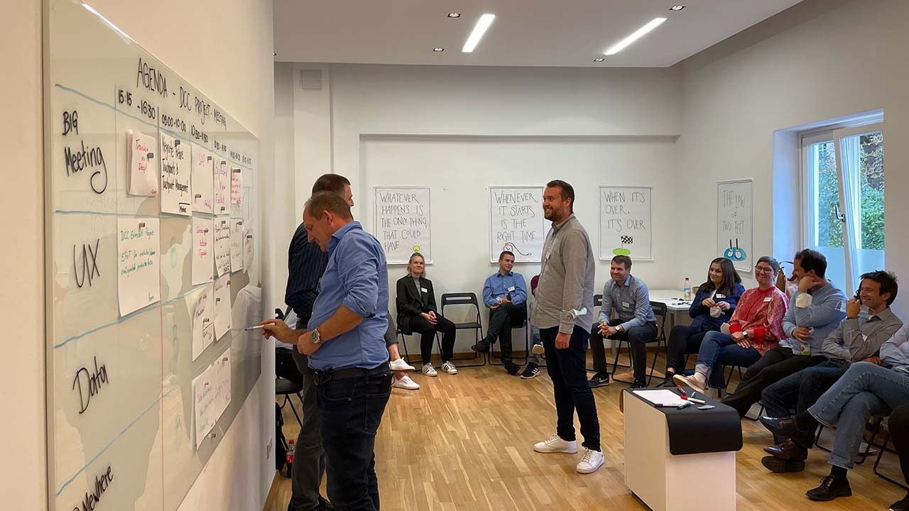 Several people sitting in a circle, looking at a board where few people are writing on.