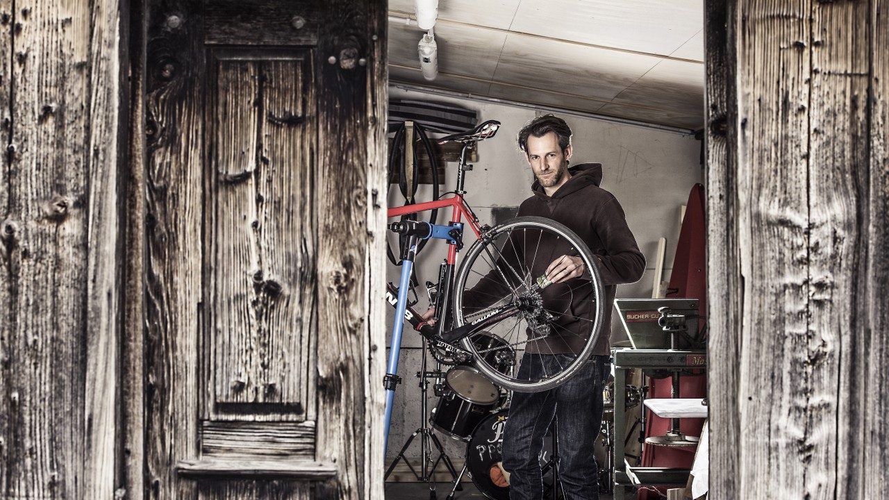 Man looks into the camera, lifting up a racing bike in a garage.