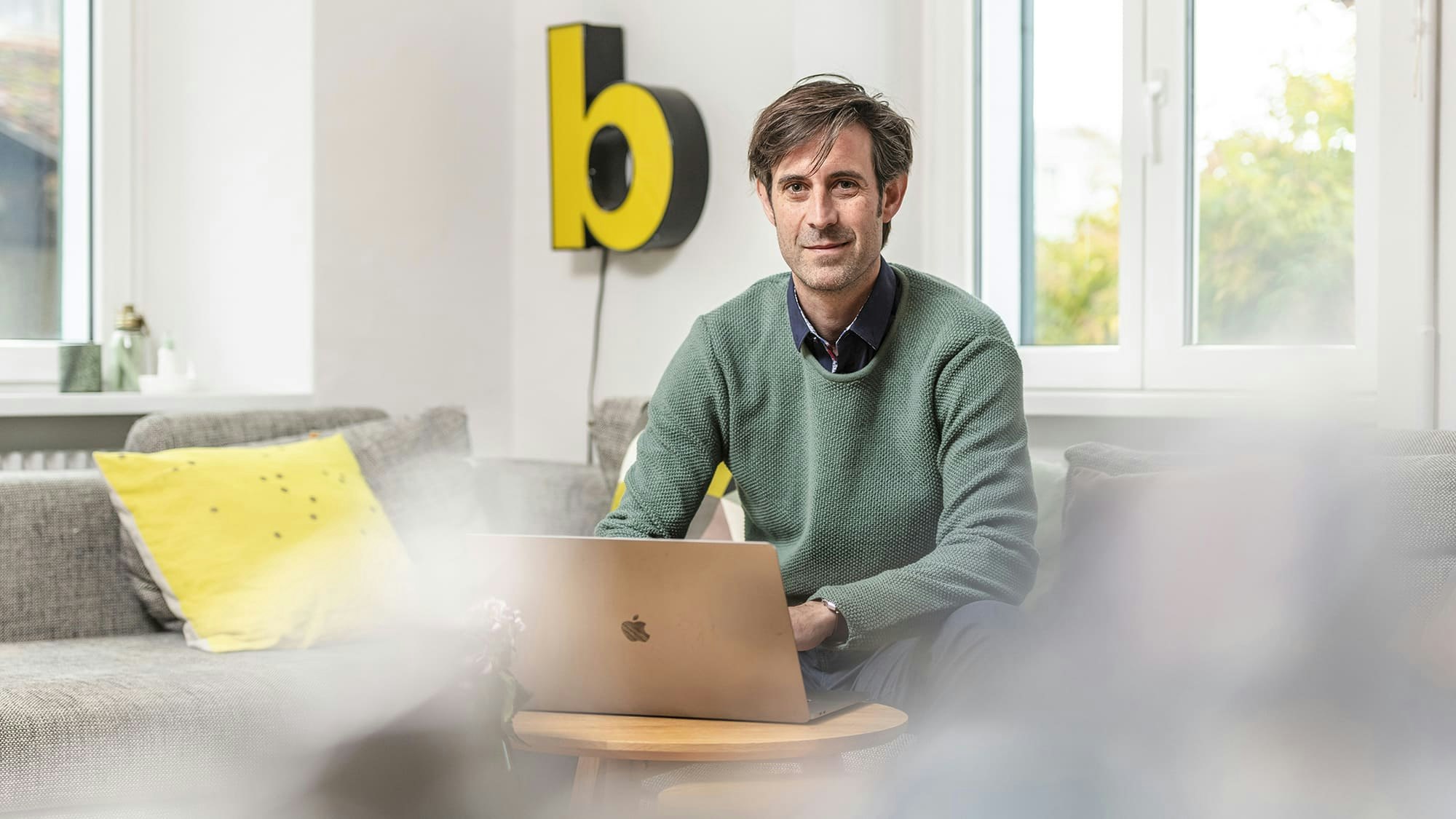 Christian in a green pullover, working on a laptop, smiling in the camera