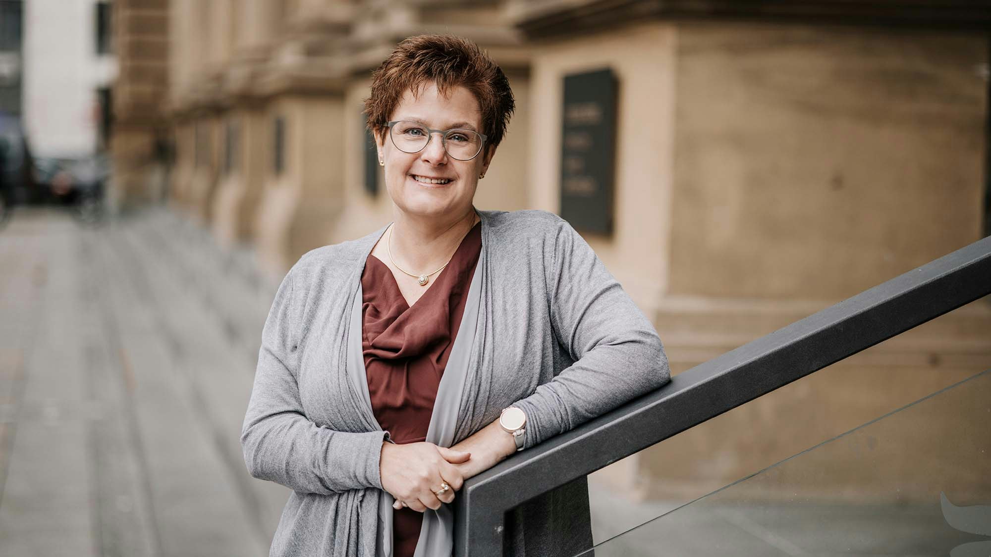 Kathryn in a dark orange shirt with a grey cardigan, smiling in the camera