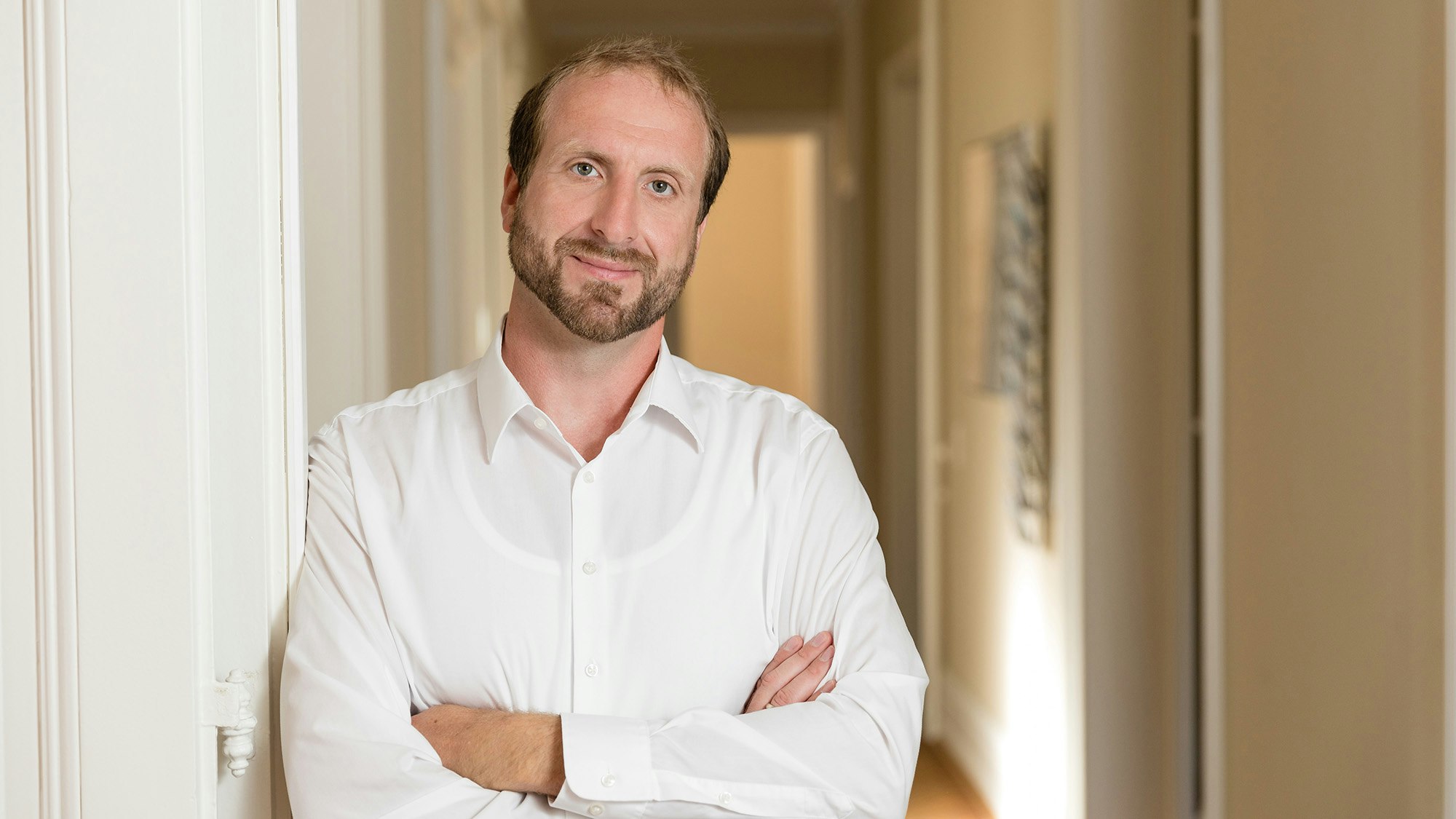 Andreas in a white shirt, leaning against a wall, smiling