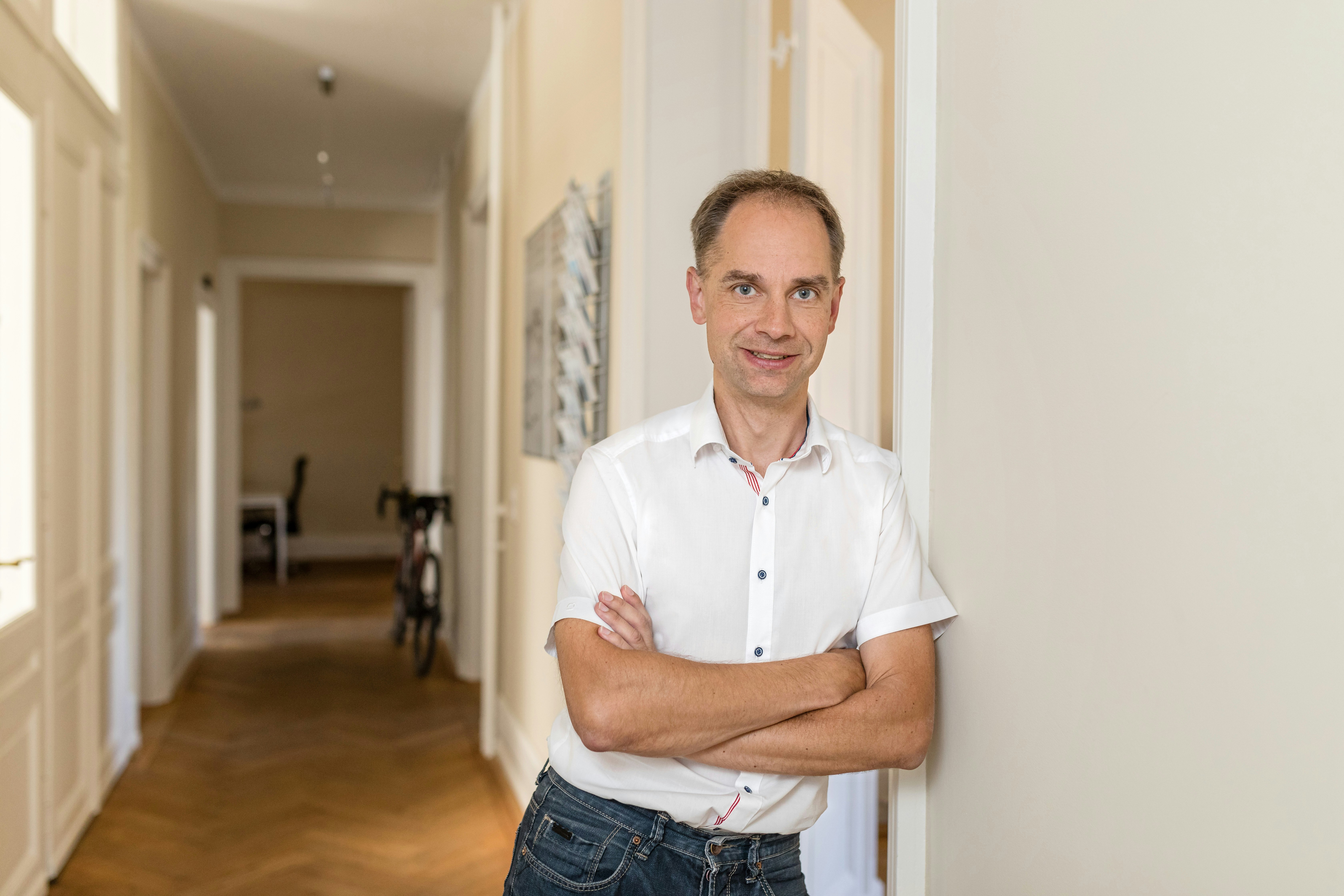 Torsten in weißem Hemd und Jeans, an eine Wand gelehnt in einem Korridor