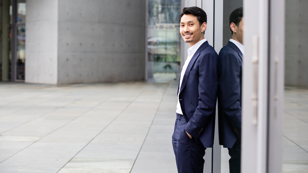 Long Do in a dark suit with white shirt is standing sideways to the camera, smiling.