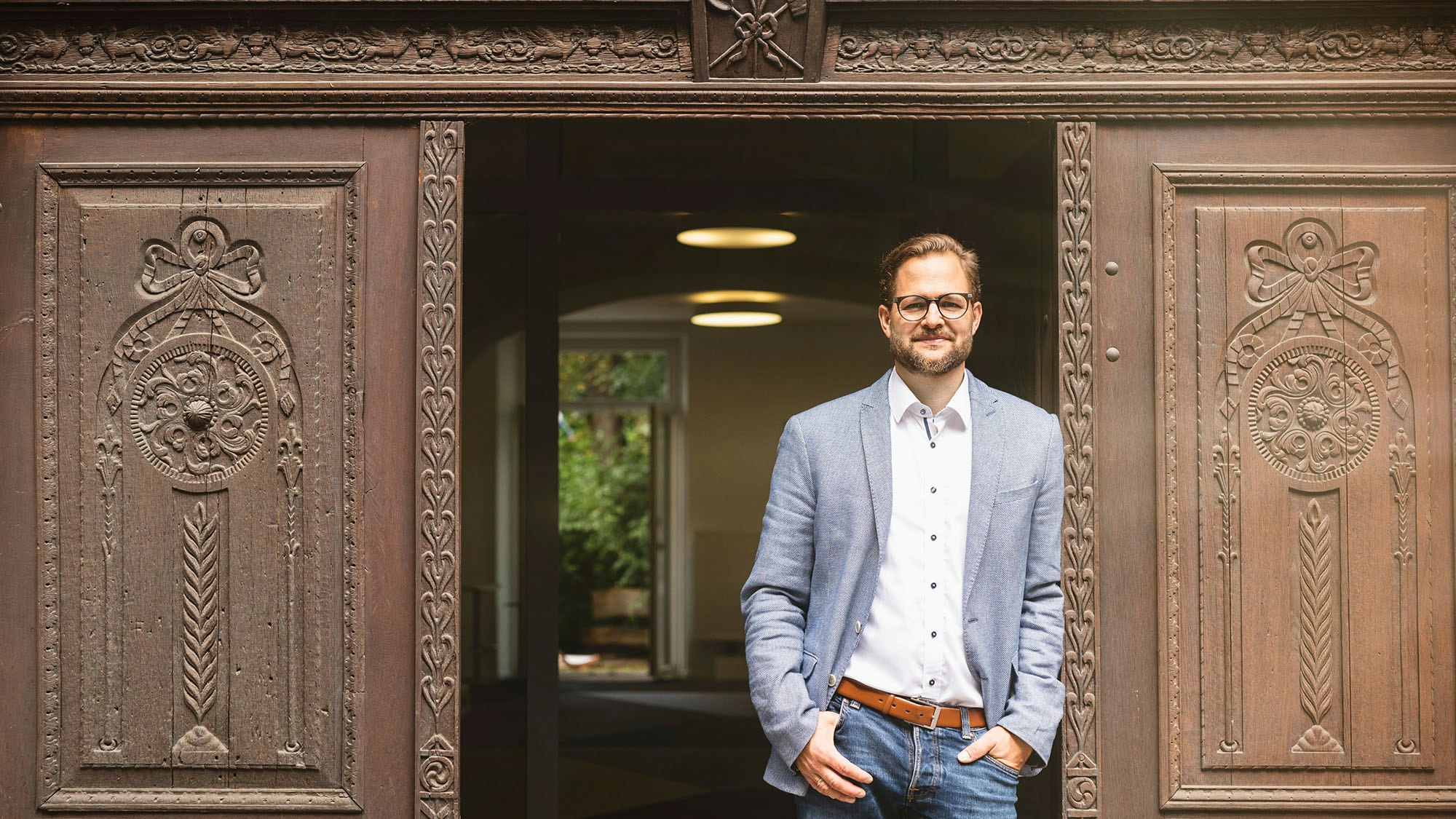 Elmar E. Grandel is standing in an entrance framed by carved wooden door.