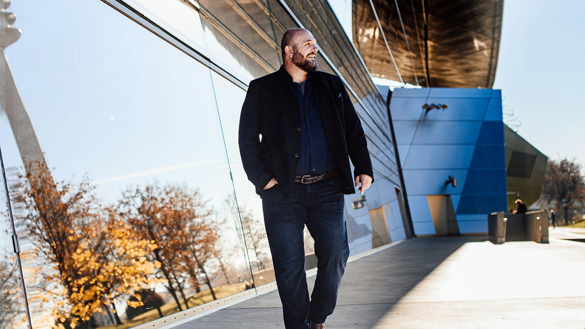 Stefan Kotulla walking with a hand in picket next to a glass mirroring wall.