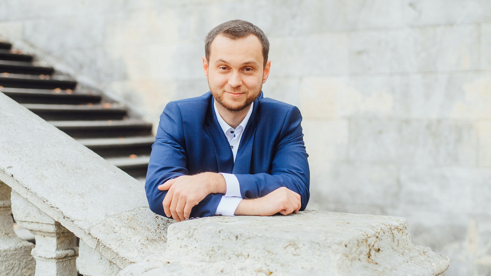 Tobias Joos standing behind a railing of a stone staircase, formally dressed.